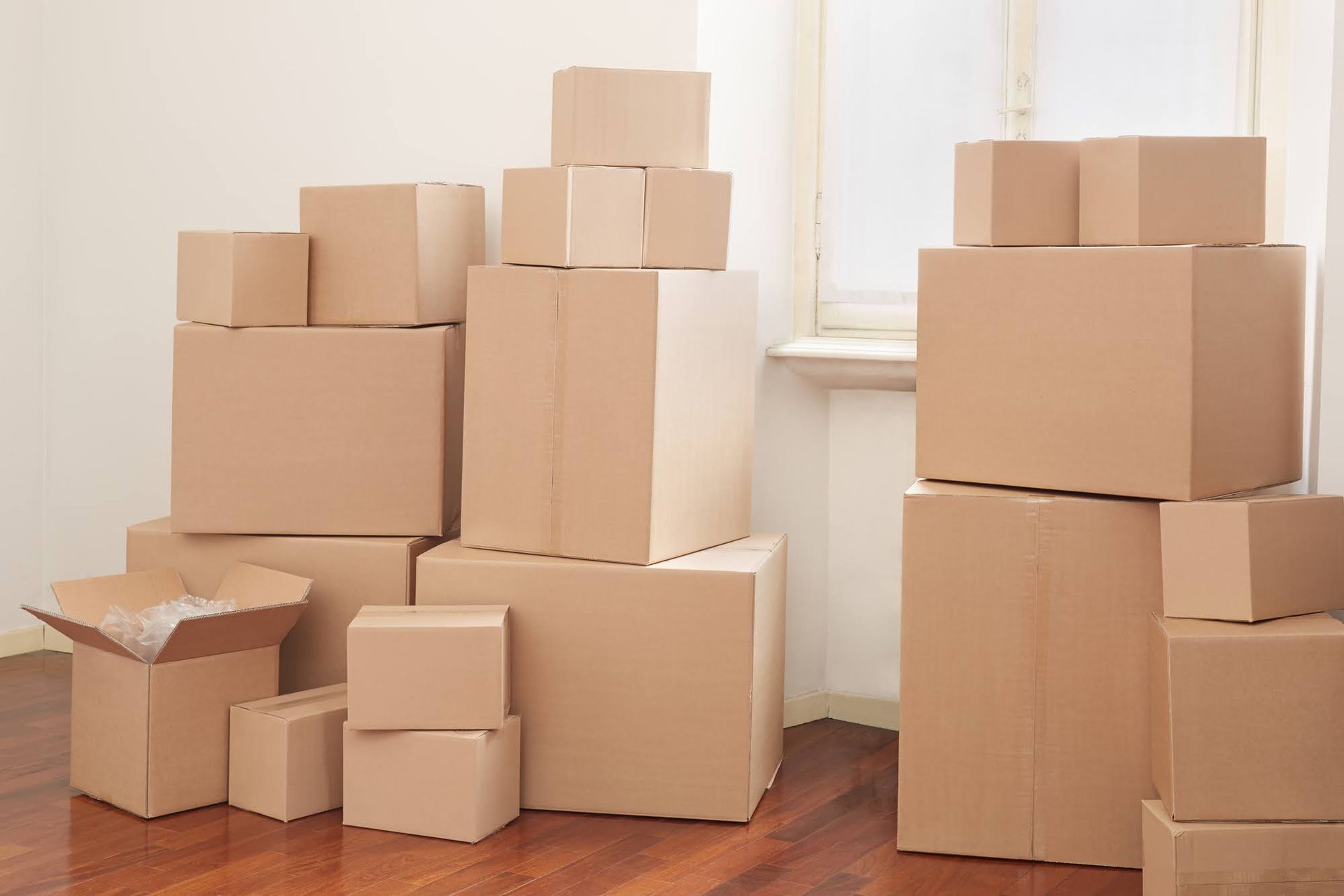 Stacks of cardboard moving boxes in a sunlit room with wooden floors.