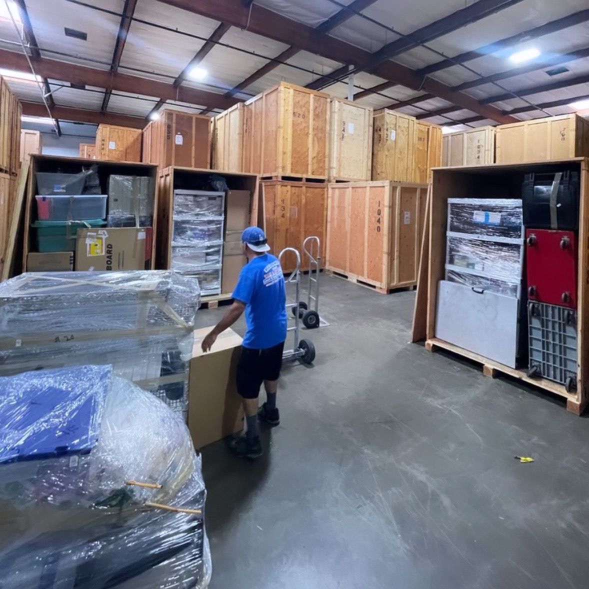 Controlled Storage - Redondo Beach, CA - Redondo Van & Storage Warehouse worker in blue shirt moving a pallet jack among stacked wooden crates and shipping containers