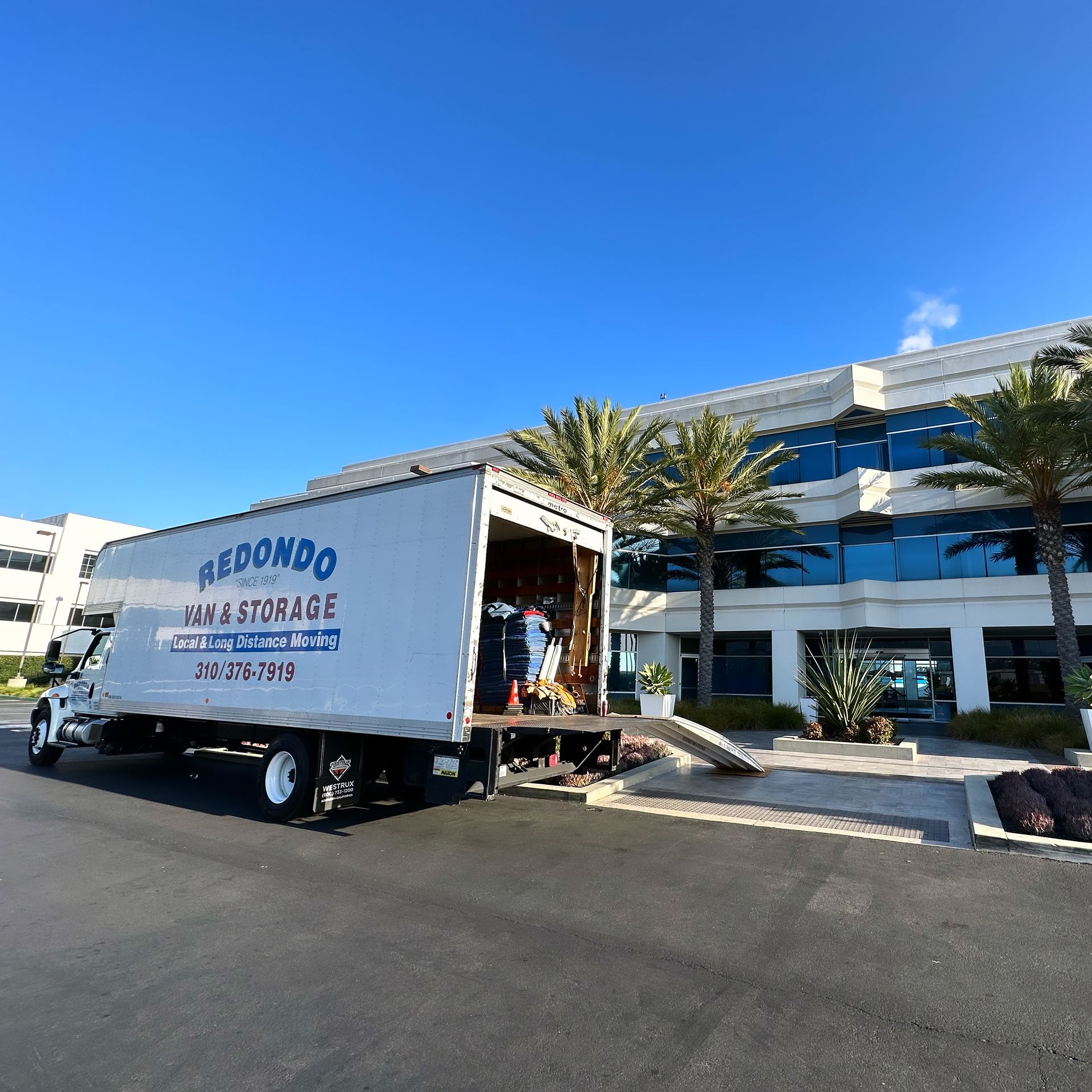 A moving truck is parked outside the building with a crew loading furniture.