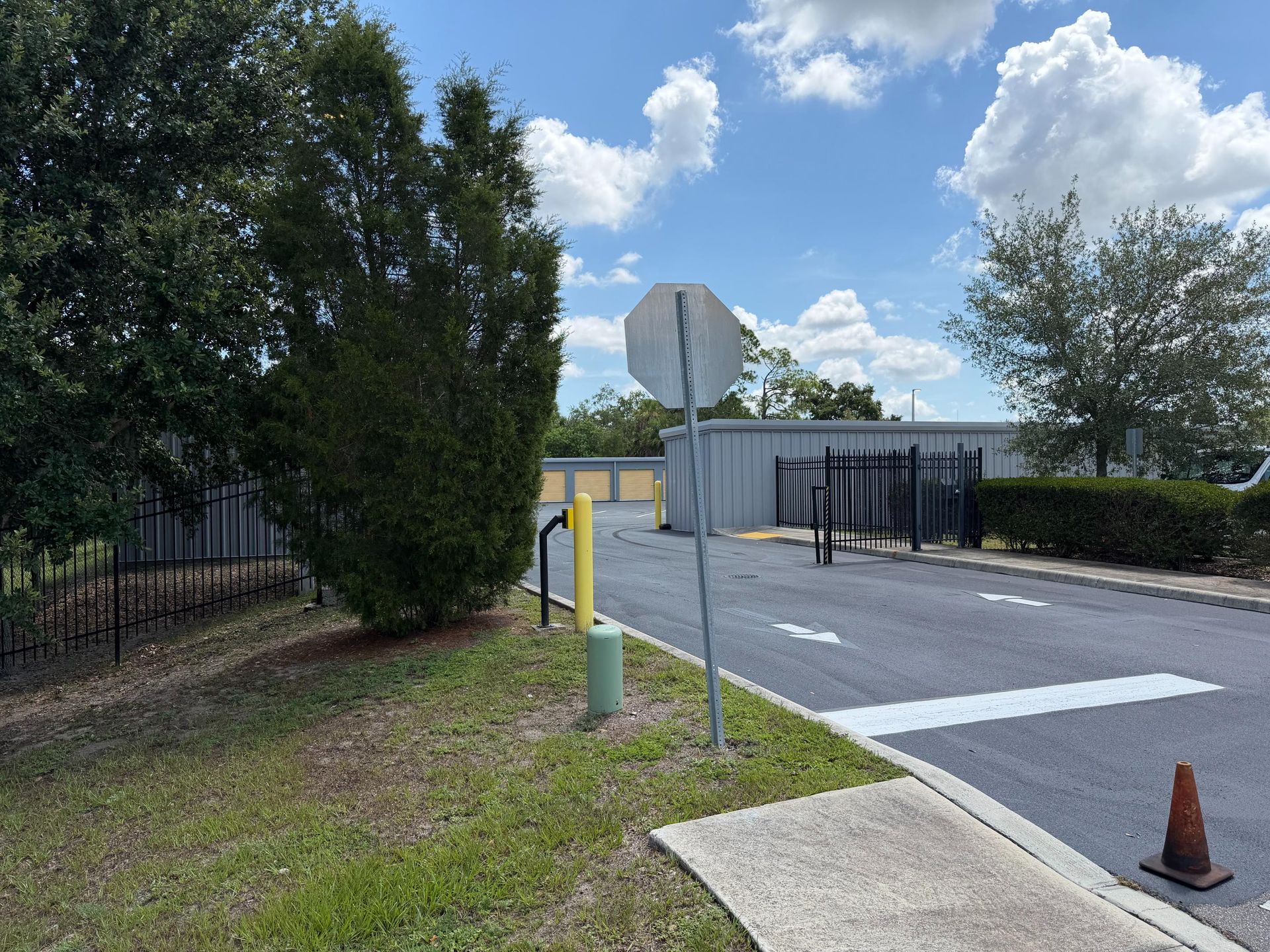Quiet road entrance with stop sign, yellow barrier, and orange cone beside trees and a building