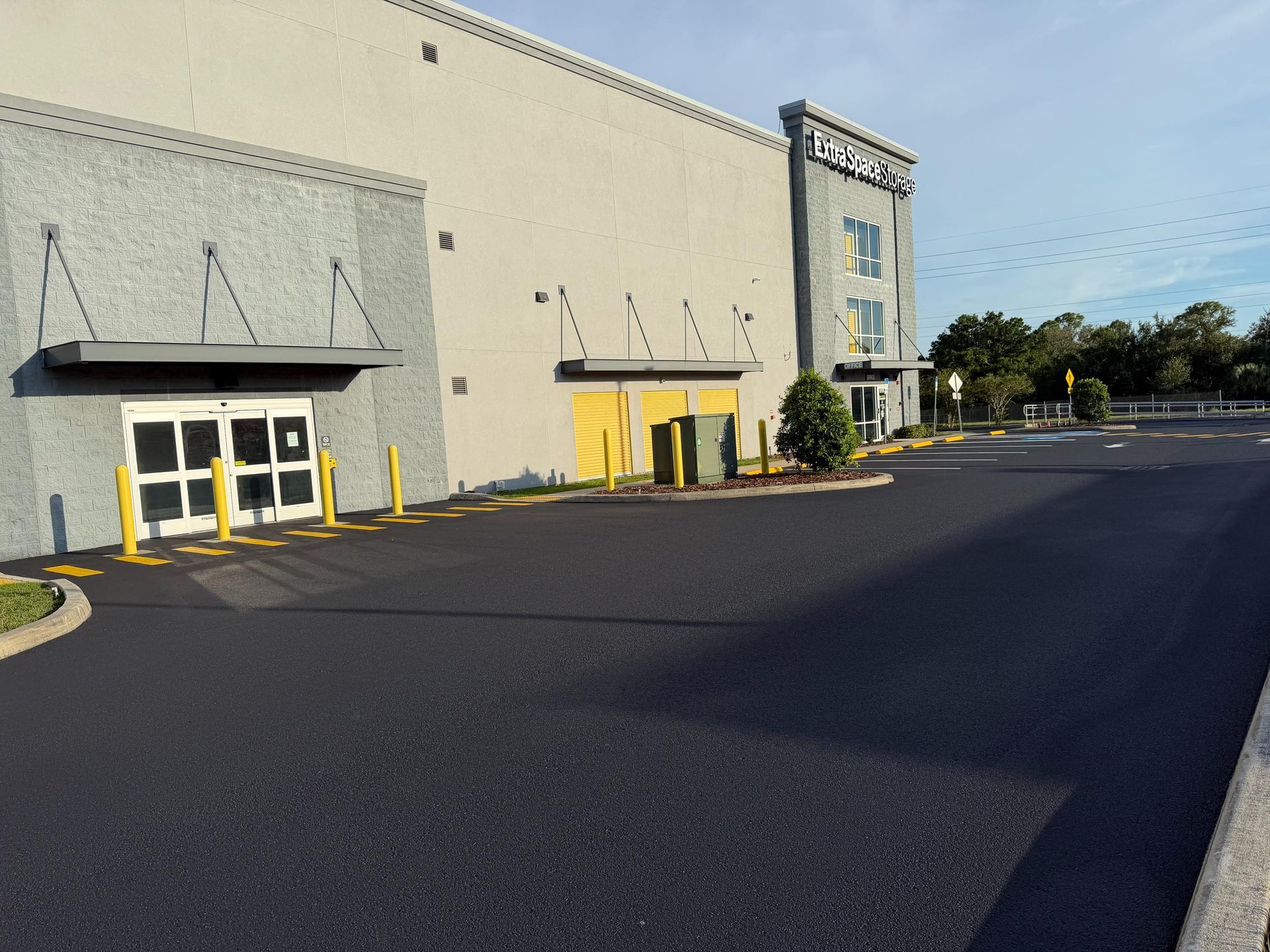 Exterior of a beige commercial building with yellow doors and a wide empty parking lot on a sunny day
