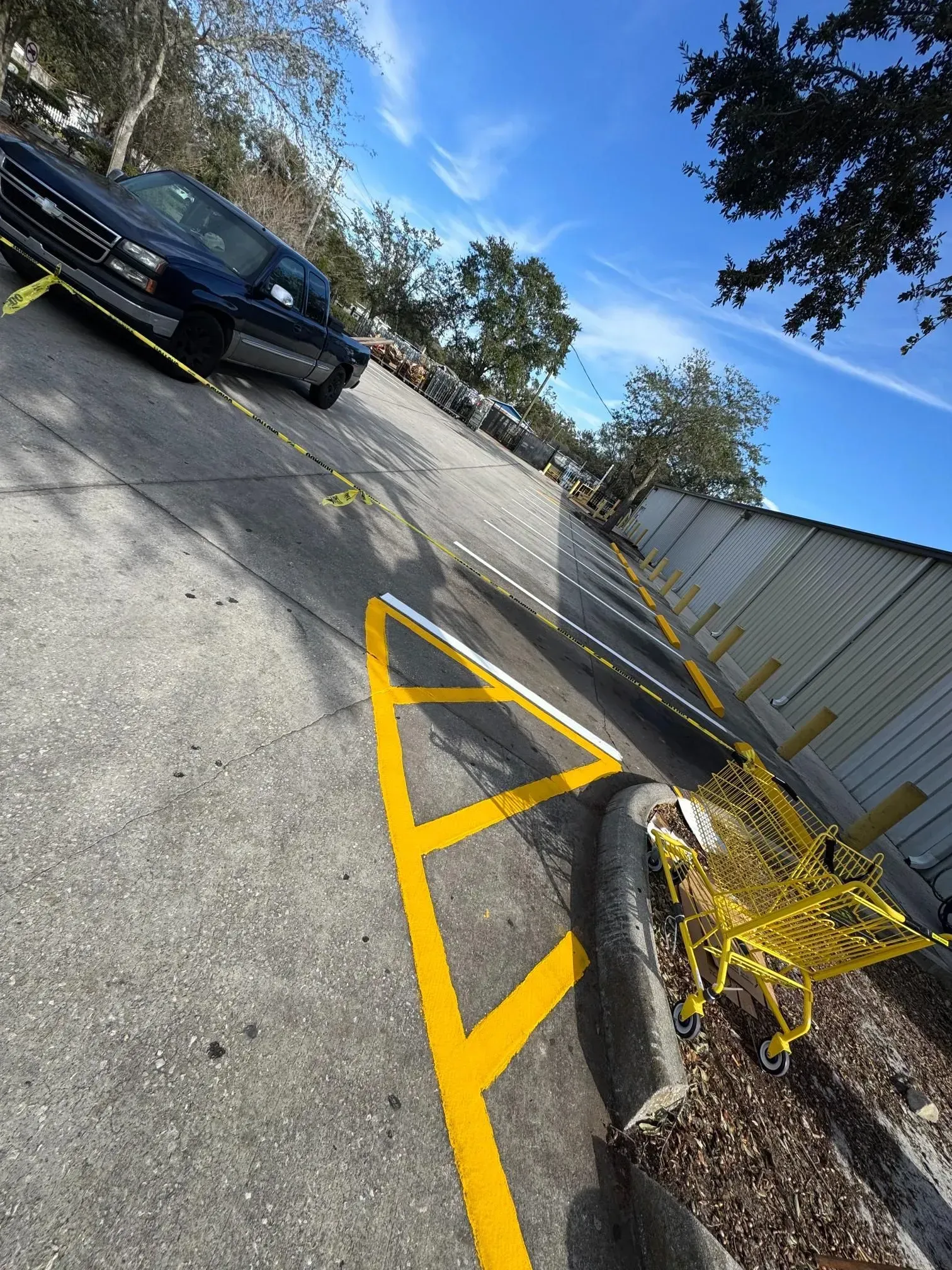 Parking lot with yellow painted curb markings, a parked black car, and a chain-link fence beside a building.