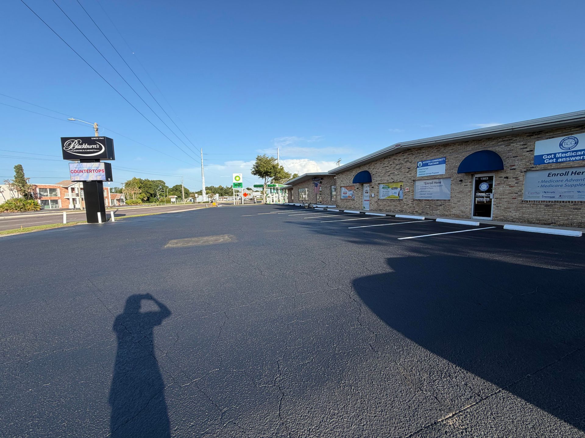 Wide parking lot beside a stone building with a sign and blue sky on a sunny day