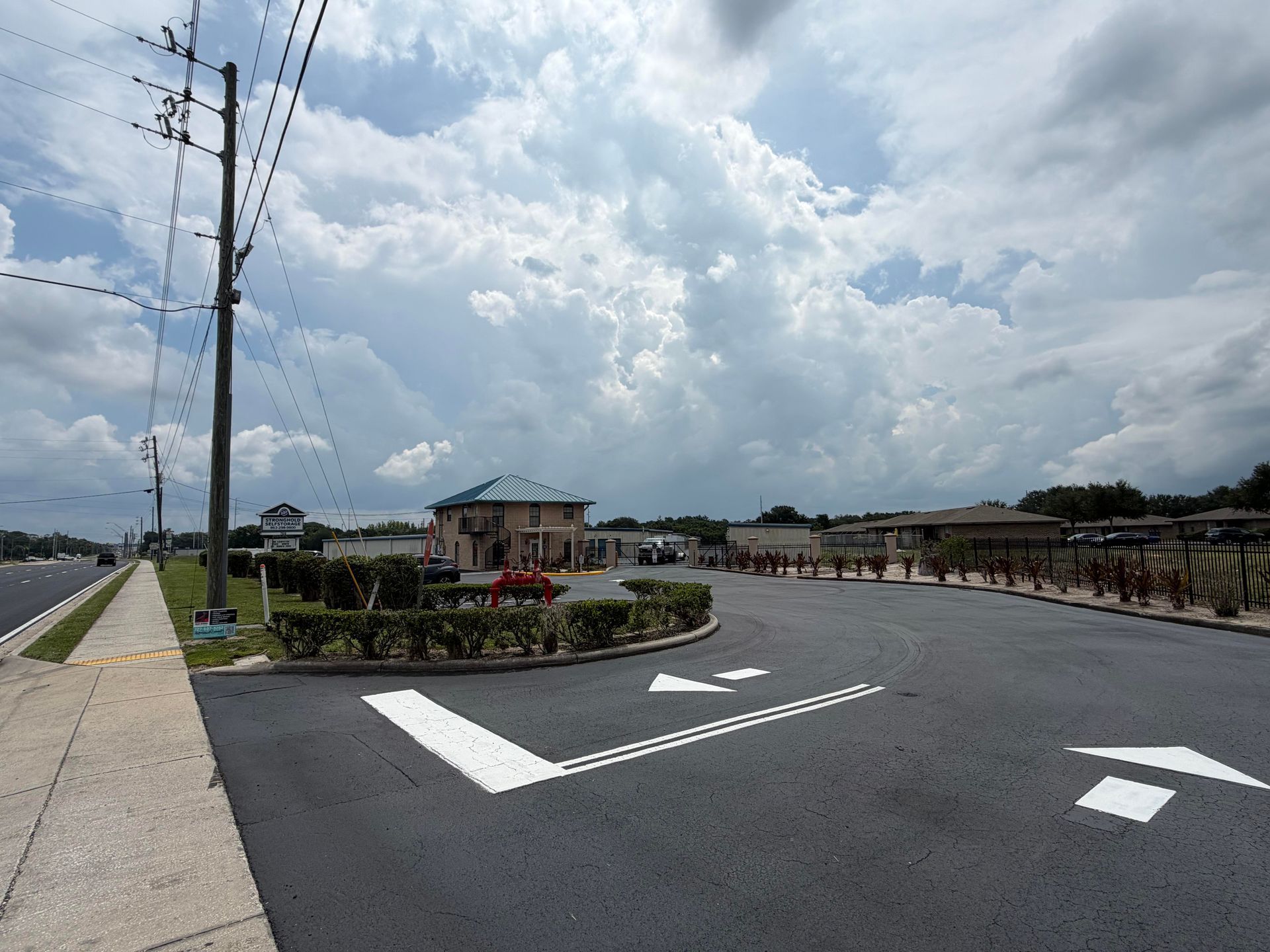 Road with directional arrows beside a landscaped entrance and buildings under a cloudy sky