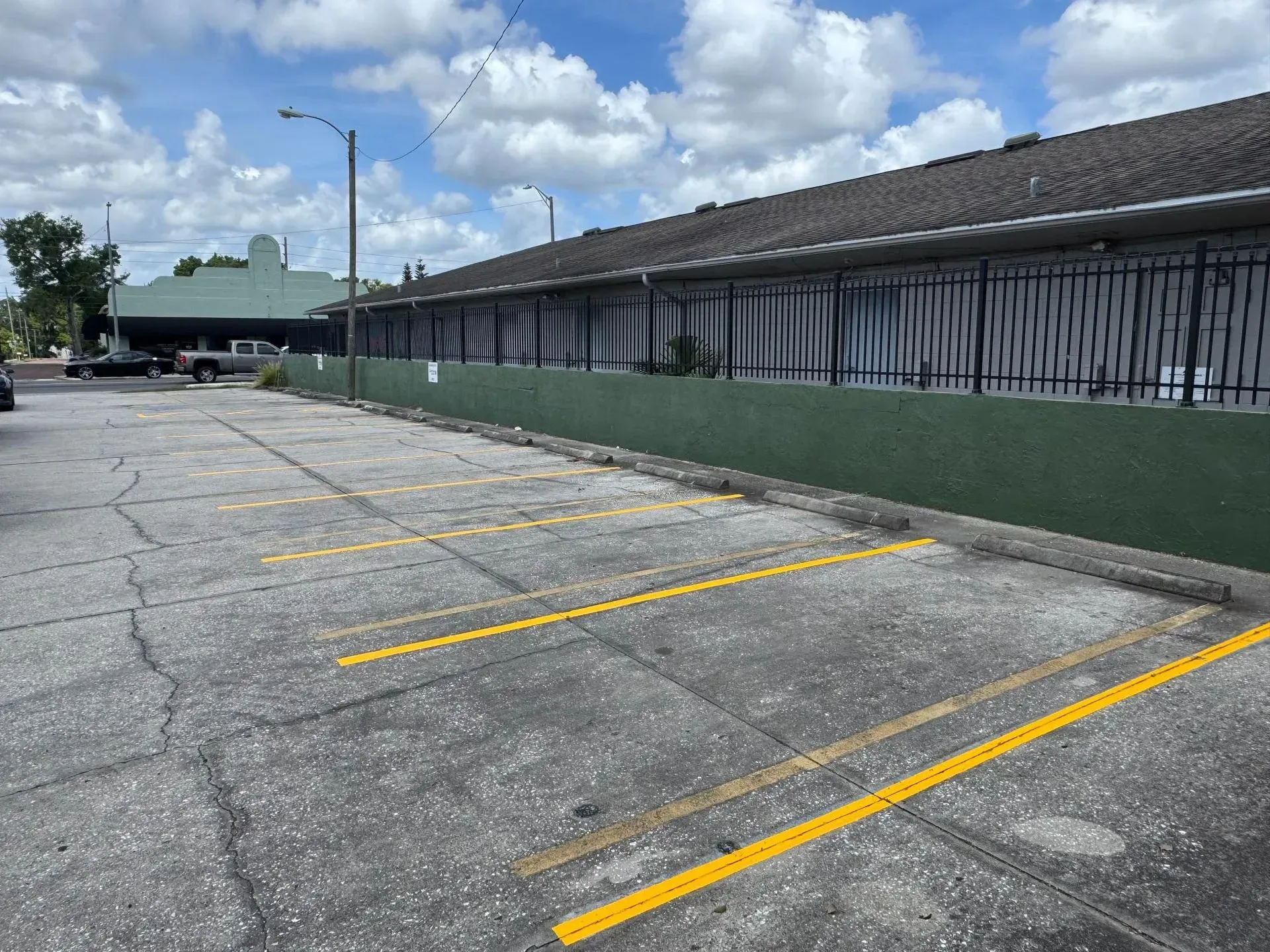 Empty parking lot beside a long green building under a cloudy sky