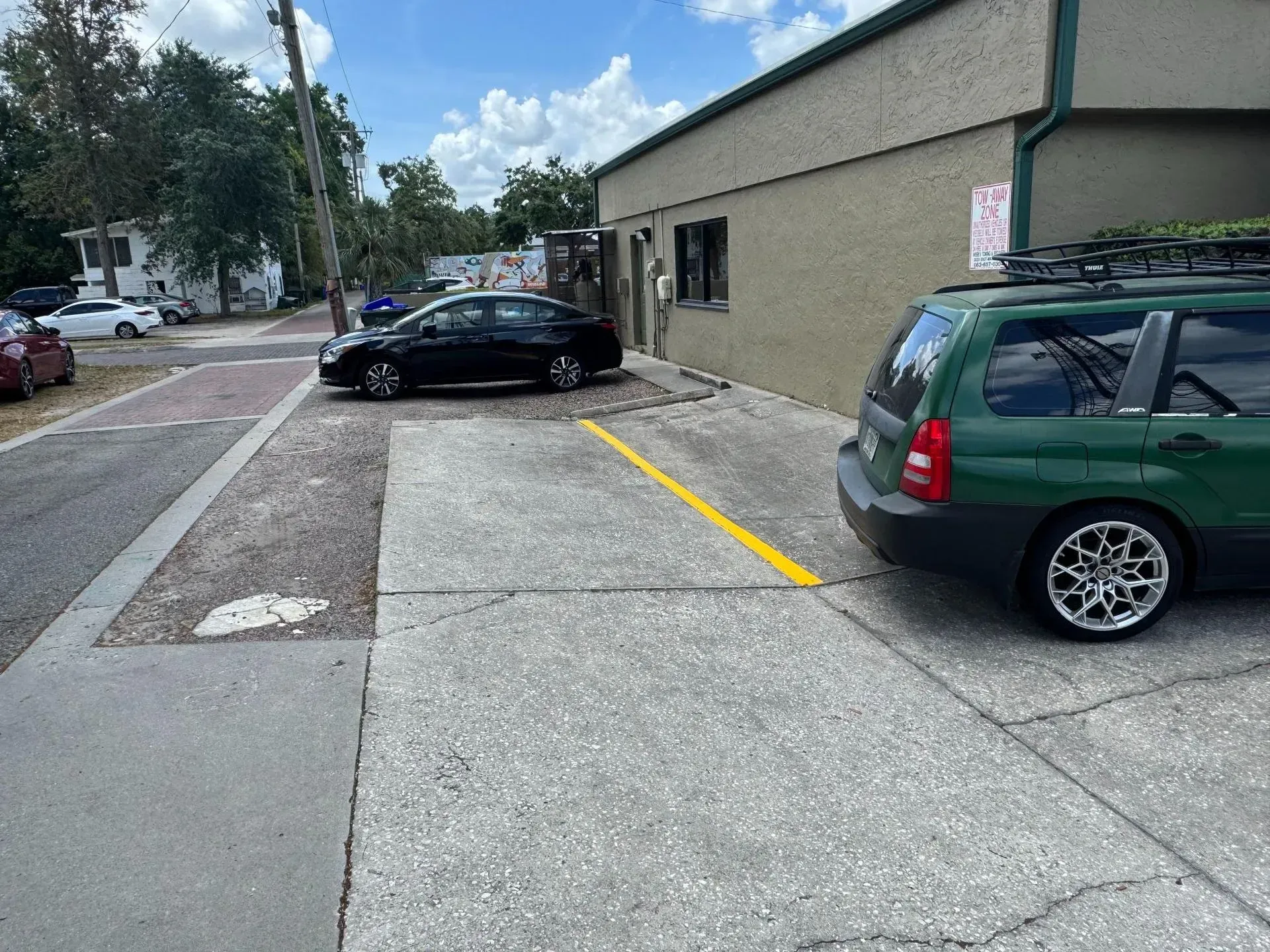 Parking lot beside a beige building with two parked cars and a yellow line marking a space