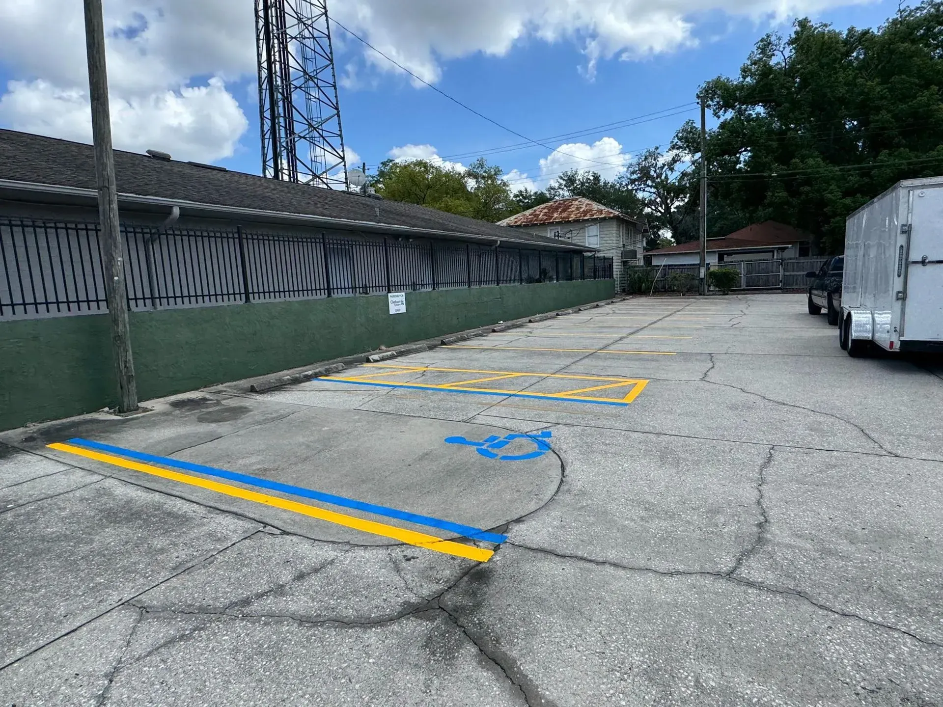 Empty cracked parking lot with blue and yellow painted markings beside a fence and white truck