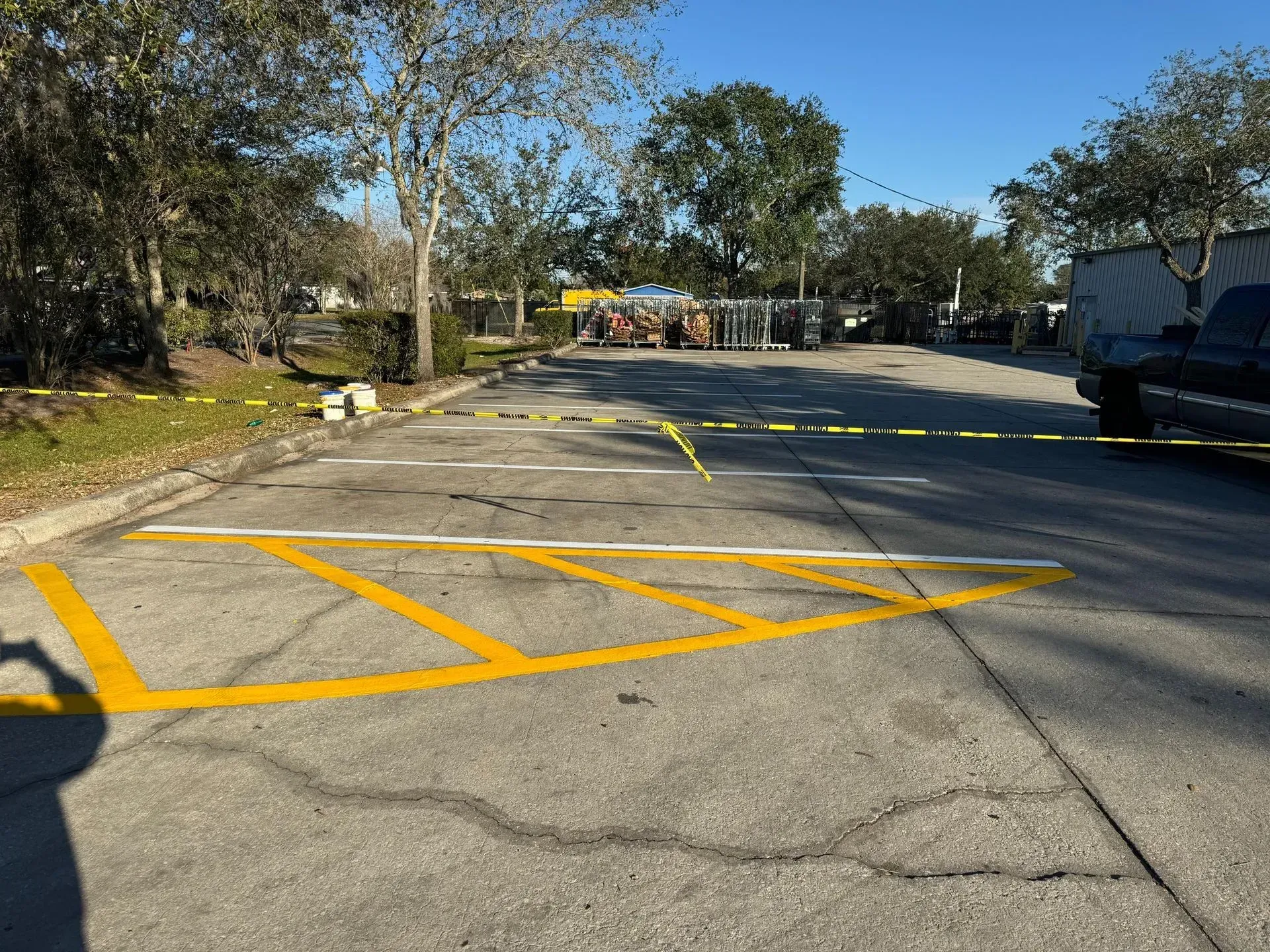 Empty parking lot with yellow painted markings, trees on the left, and a truck on the right.