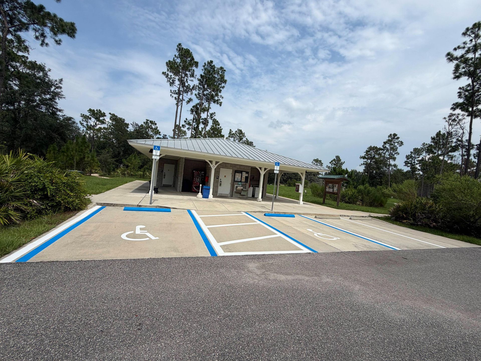Accessible parking spaces in front of a small building with a covered entrance, surrounded by trees.