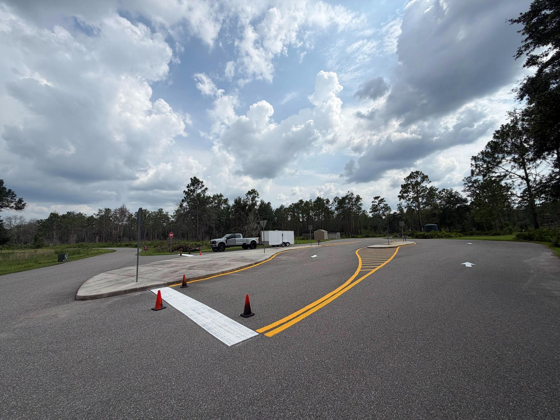 Traffic training lot with cones, painted lane markings, and cloudy sky over trees