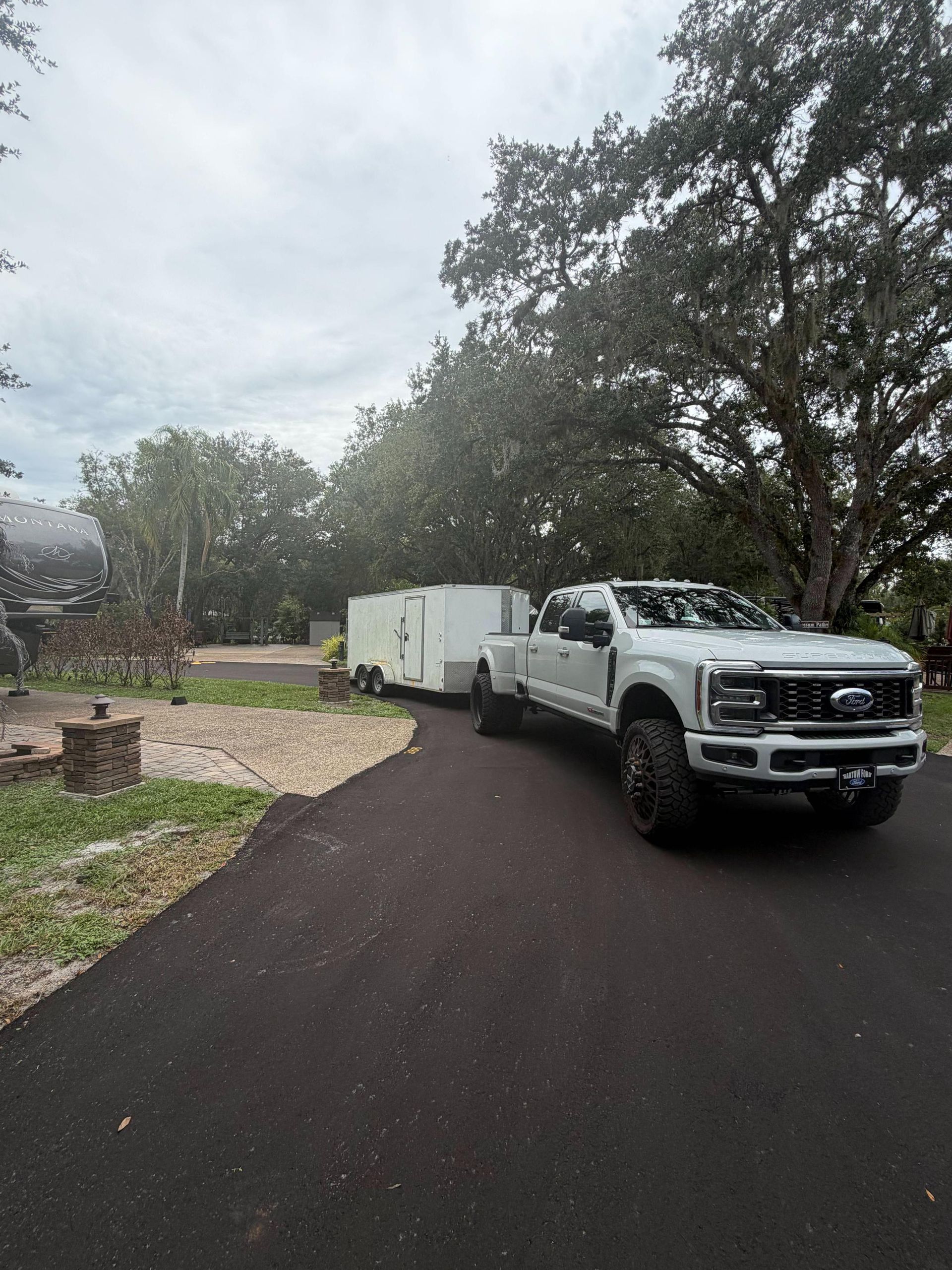 White pickup truck with enclosed trailer parked on a dark driveway beside trees and a house
