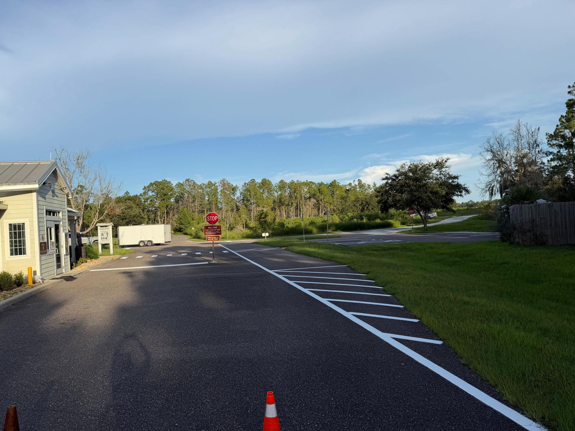 Curved empty road beside a building and grass, with orange cones and trees under a blue sky