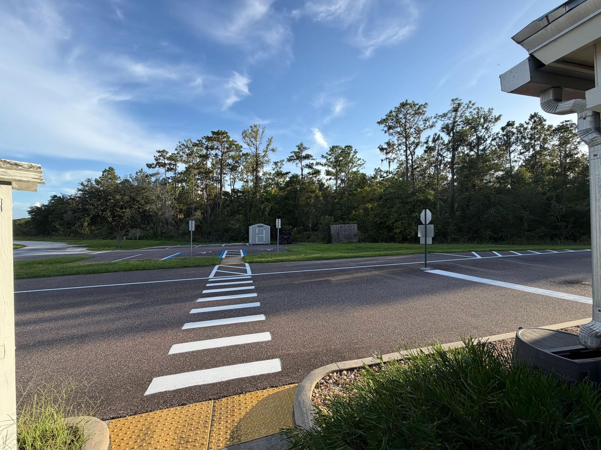 Crosswalk leading to a road intersection beside trees and a grassy verge under a blue sky