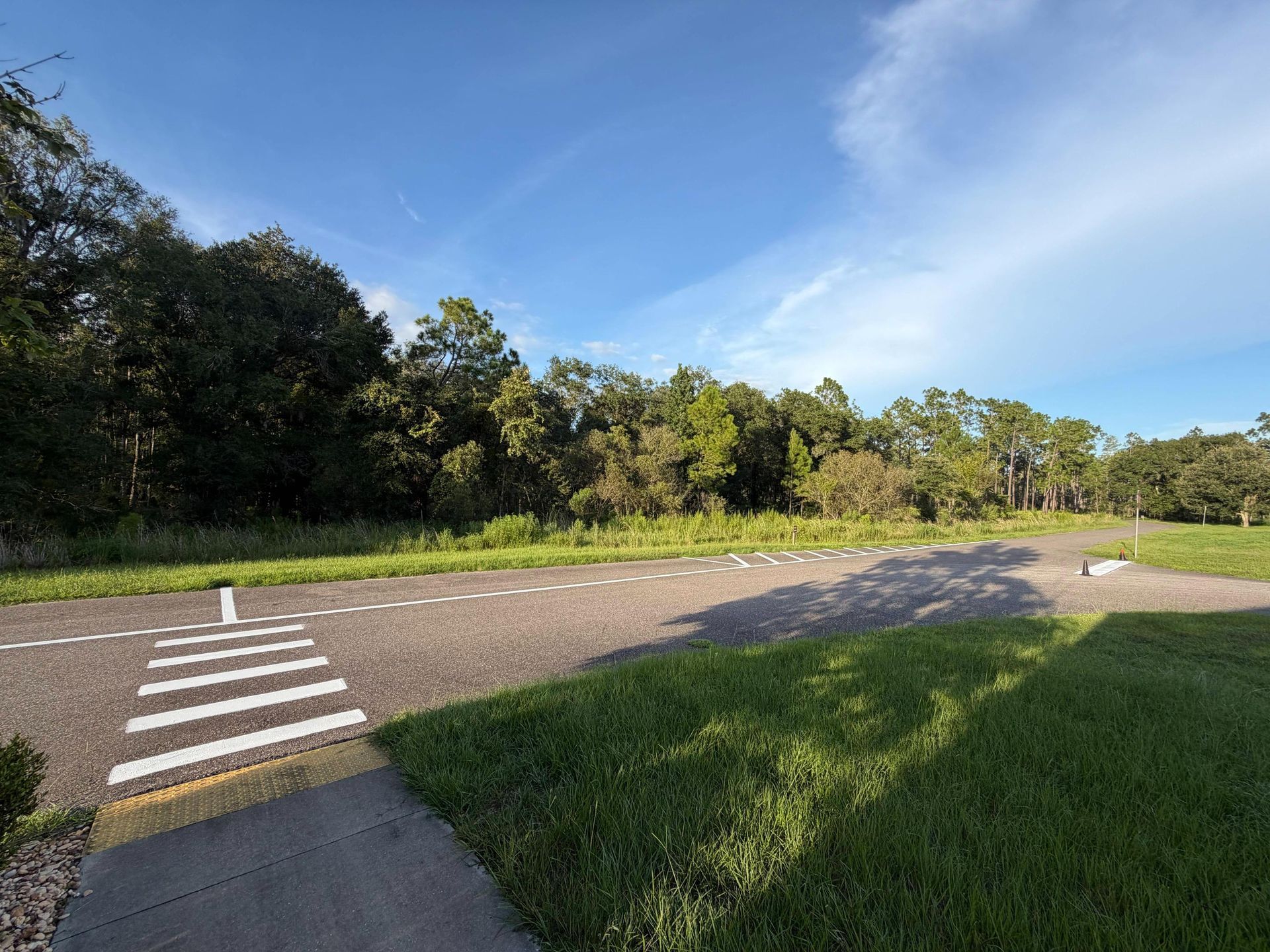 Crosswalk beside a paved path curving through a sunny green park under a blue sky