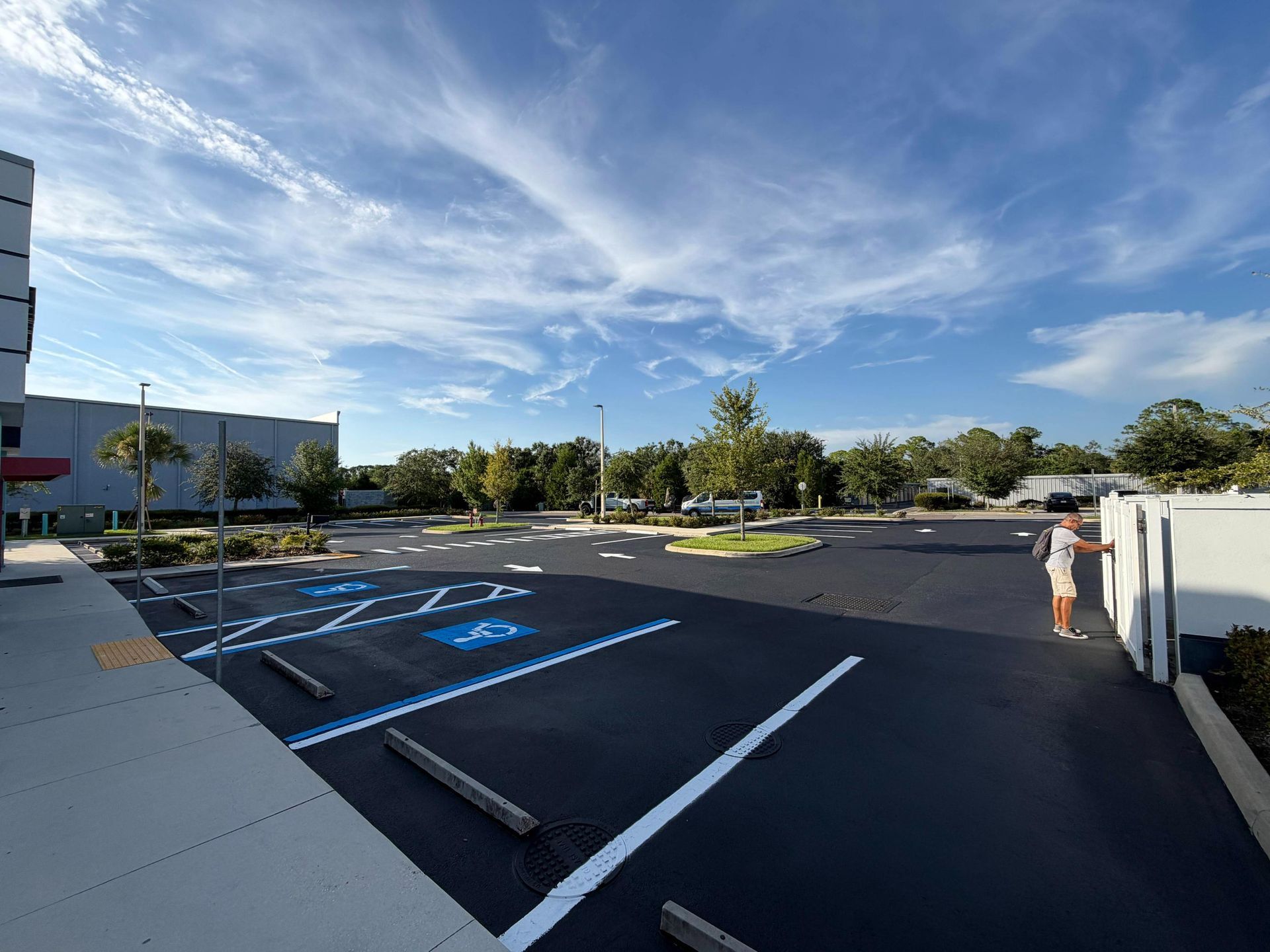 Accessible parking lot with blue spaces and a person walking near a white fence under a sunny sky