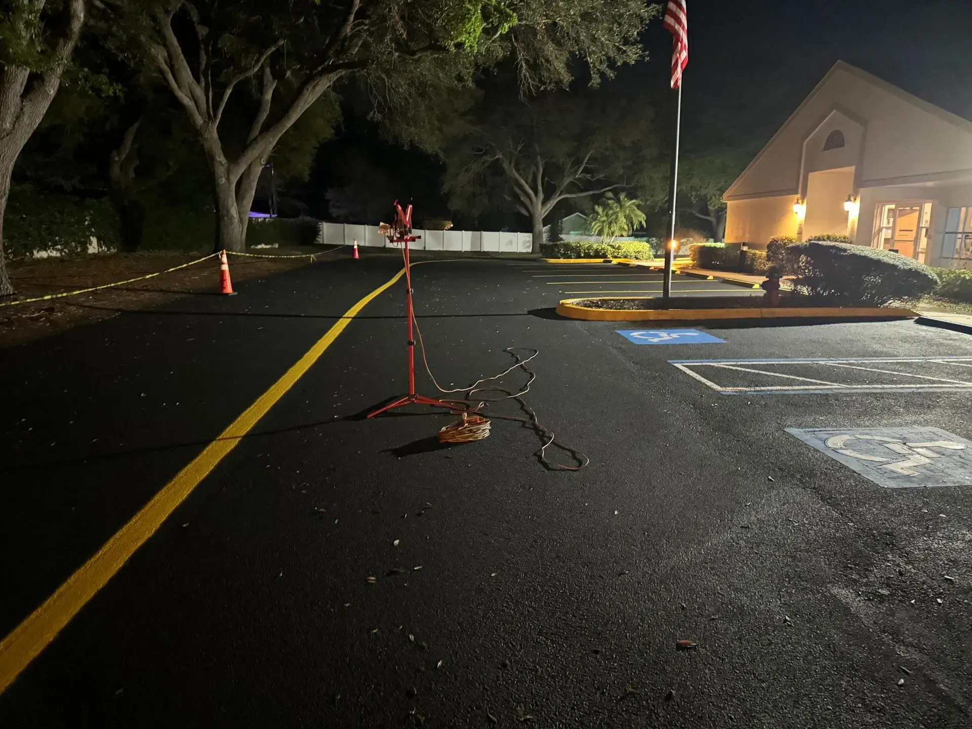 Nighttime road closure with orange cones and caution tape on a wet parking lot near a lit building