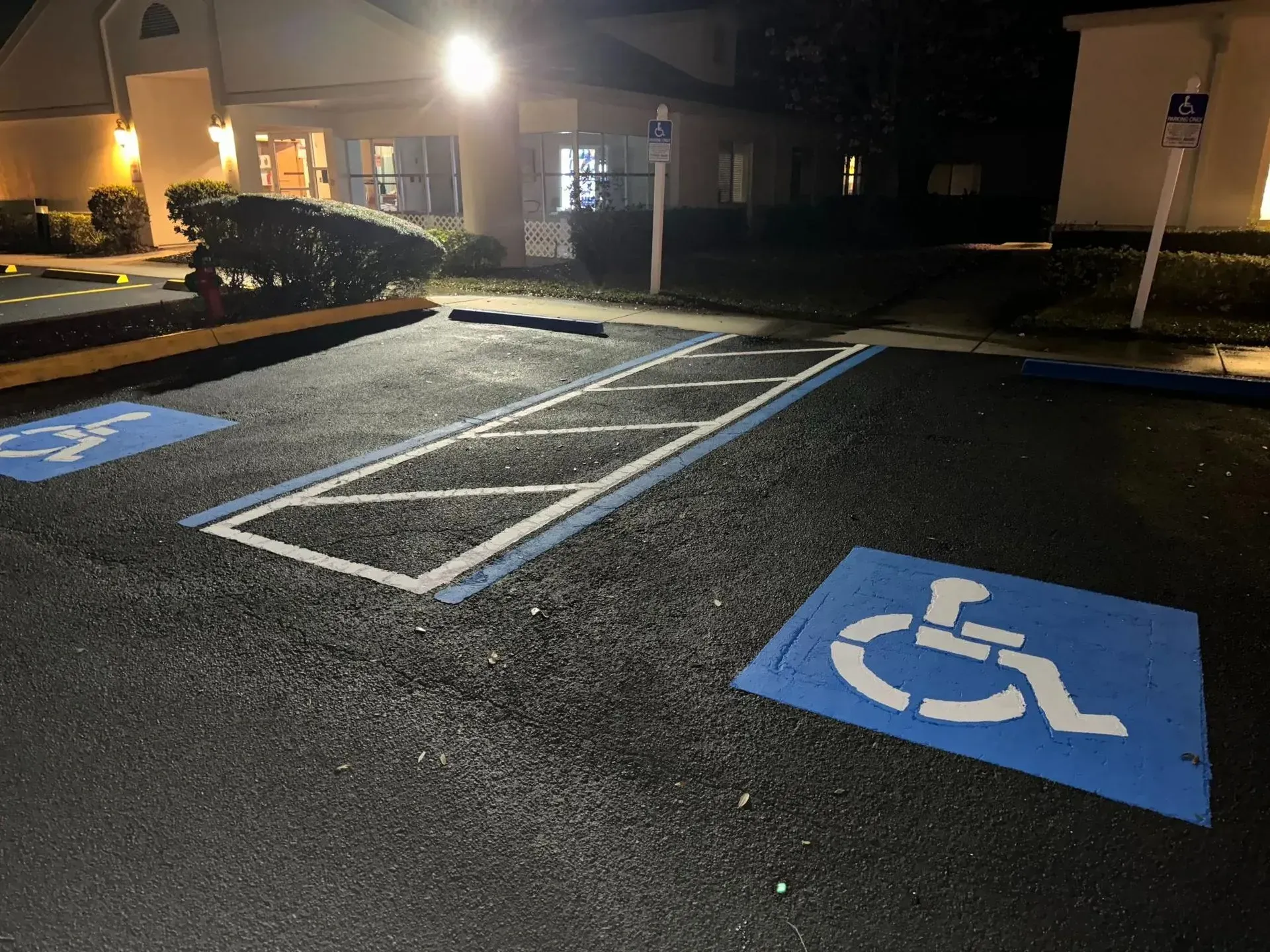 Nighttime accessible parking lot with blue handicap spaces and striped loading zone near a building entrance