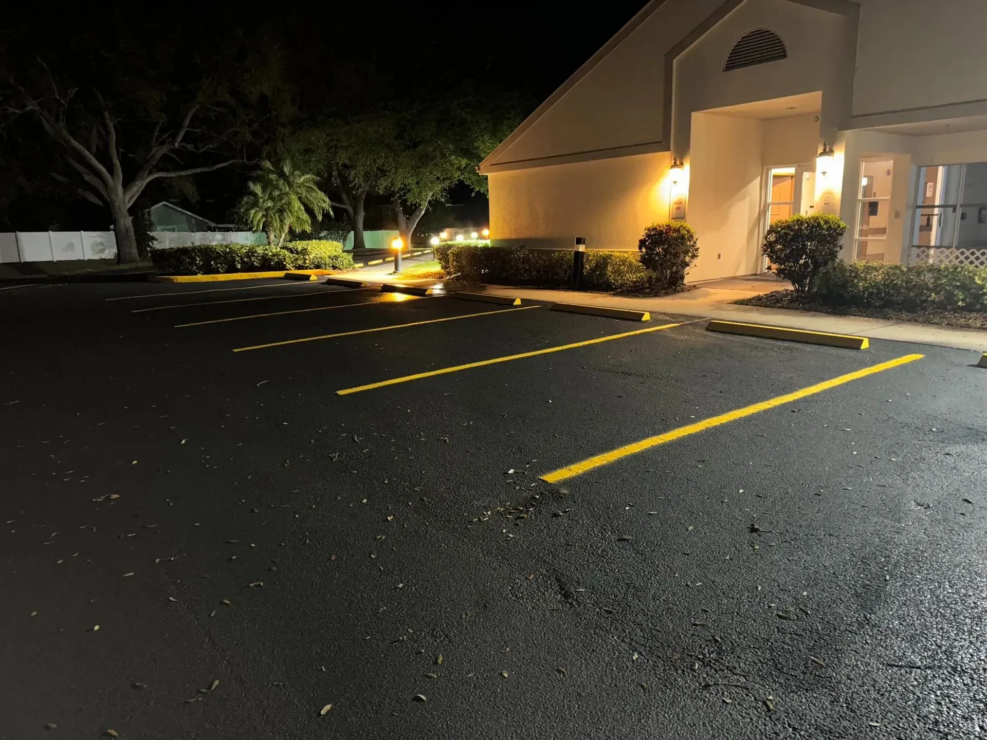 Nighttime parking lot beside a lit building entrance and yellow parking lines