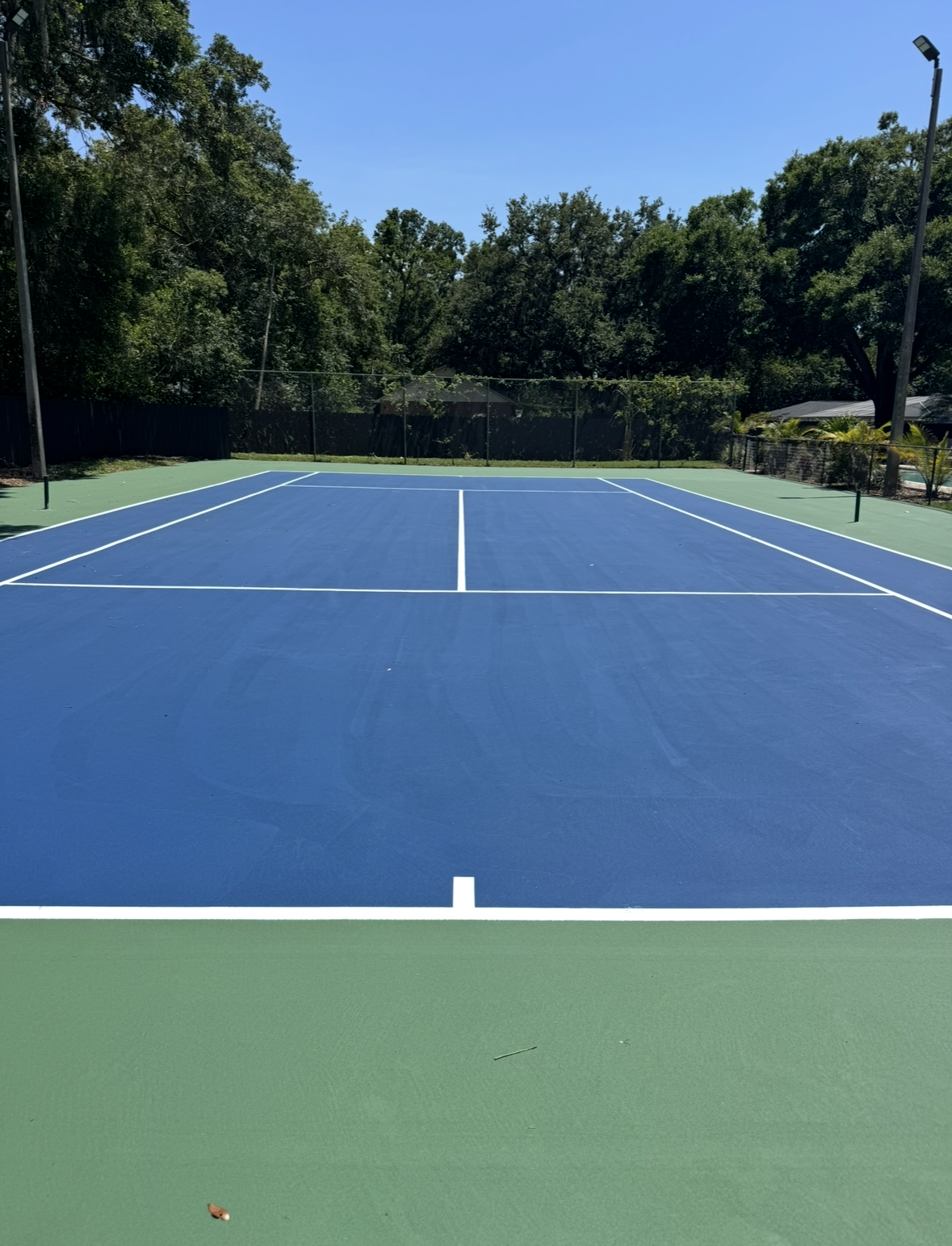 Blue and green tennis court under clear sky, with trees in the background