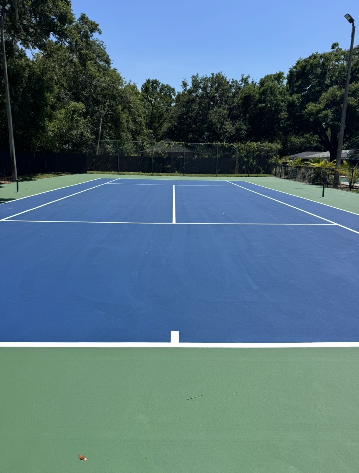 Blue outdoor tennis court surrounded by trees under clear sky
