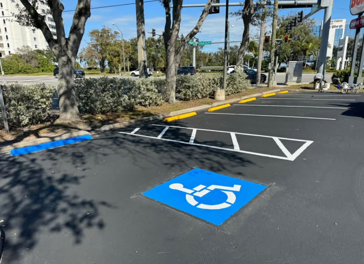 Accessible parking spaces with blue wheelchair symbols in a paved lot under trees.