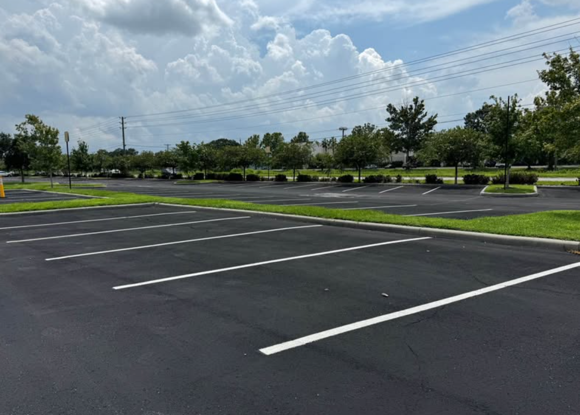 Empty parking lot with freshly painted white lines beside a grassy median and palm trees under a cloudy sky