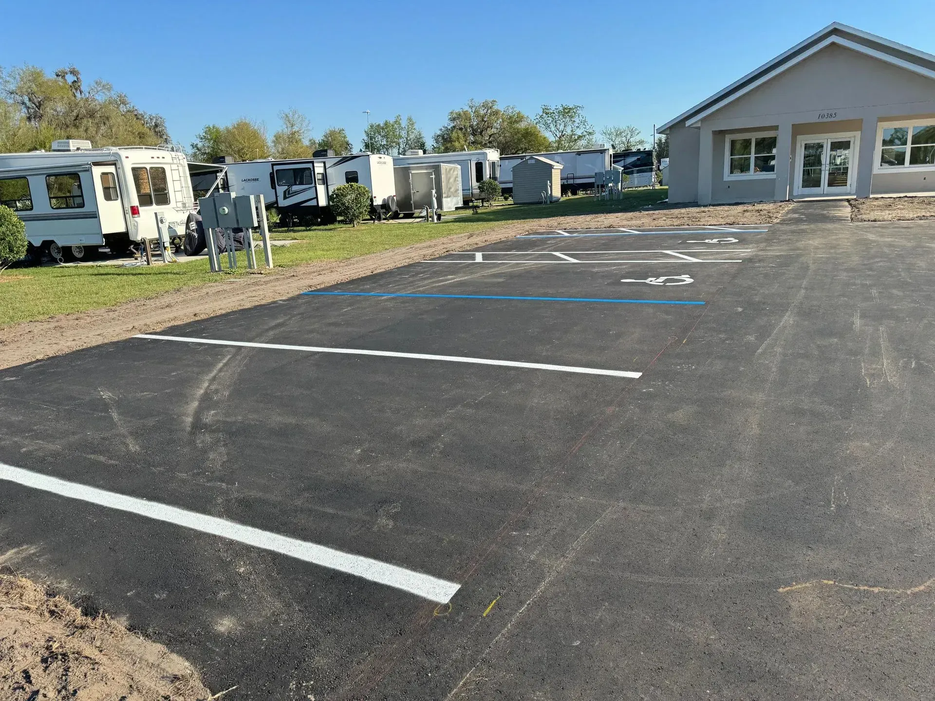 Empty paved parking lot with white lines beside a small building and RVs under a clear sky