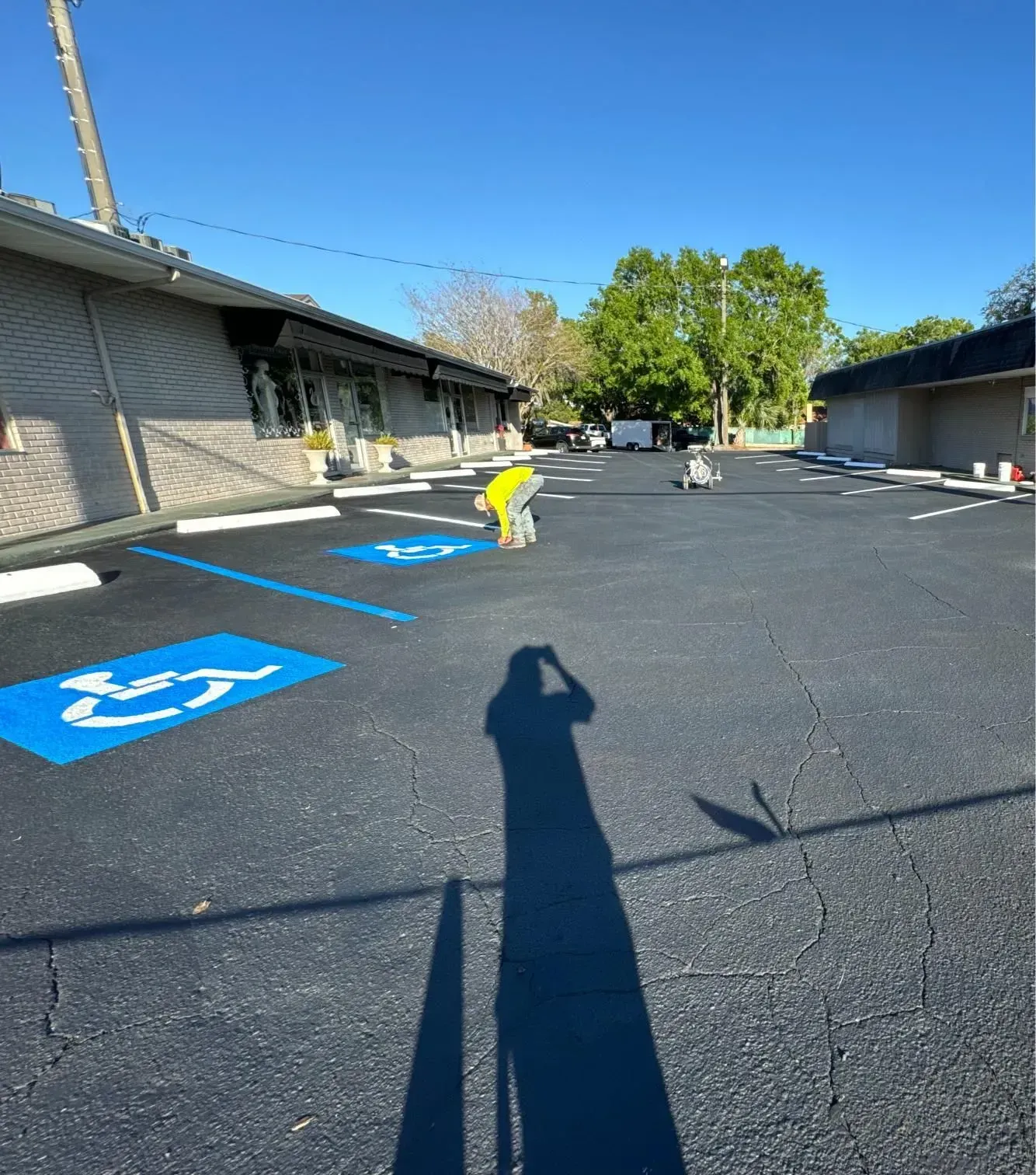 Accessible parking spaces and building walkway beside a blacktop lot under a clear blue sky