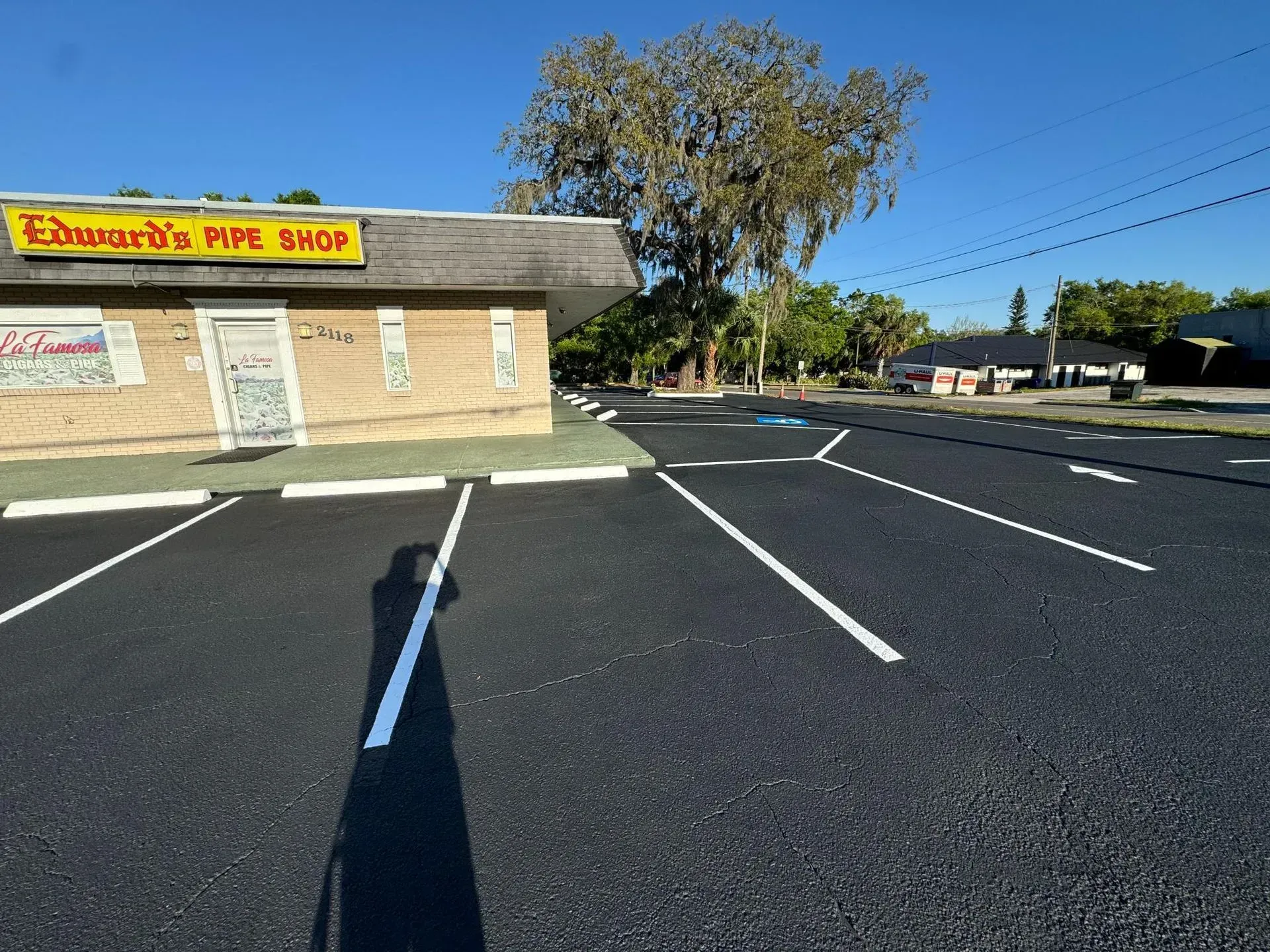 Empty parking lot beside a storefront with a yellow sign and trees in the background