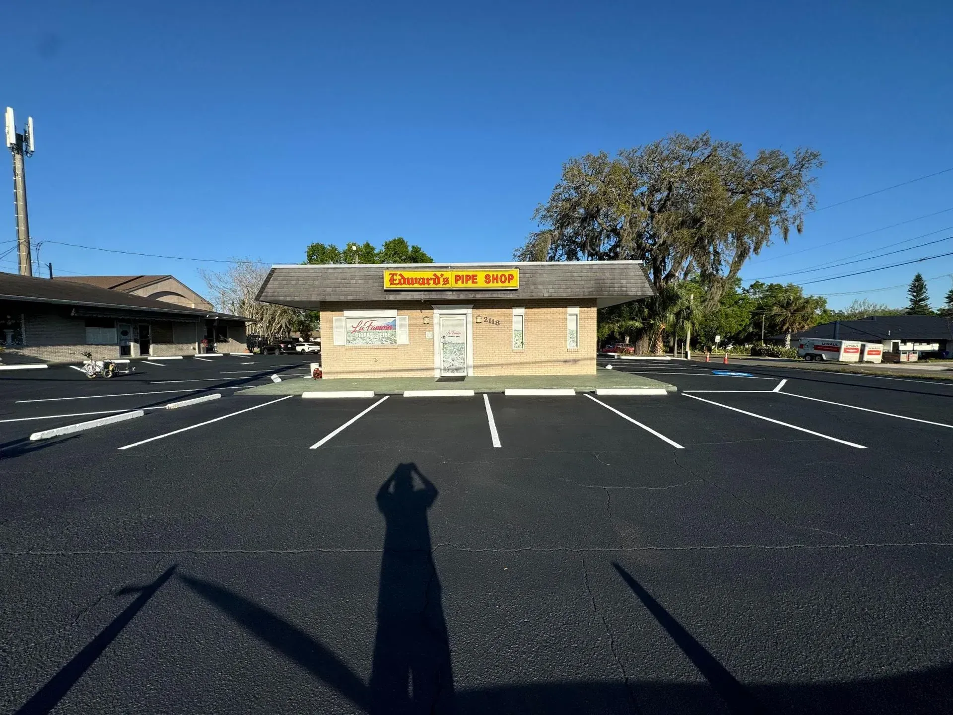 Small beige storefront with yellow sign across an empty parking lot under a clear blue sky.