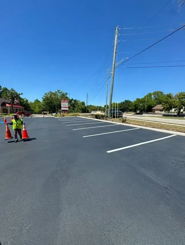 Road work with two workers and orange cones on a freshly paved street under a clear blue sky