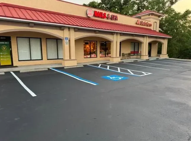 Storefront with empty accessible parking spaces in front of a beige strip mall at dusk