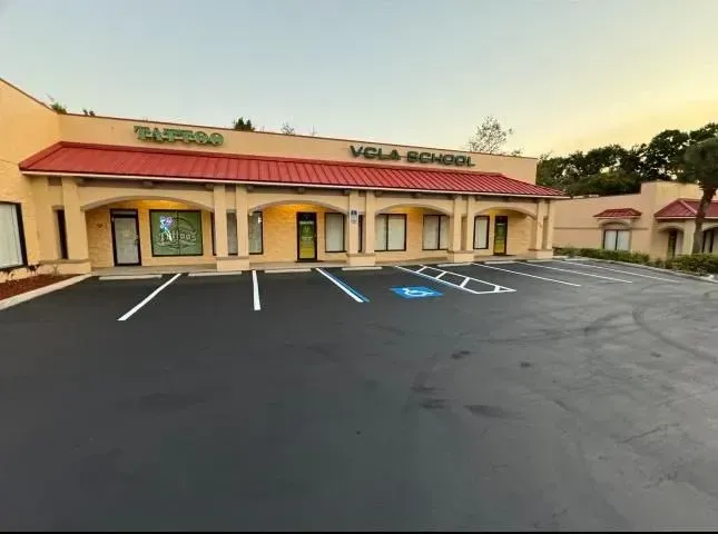 Strip mall storefront with tan stucco, red roof, and empty parking spaces at sunset