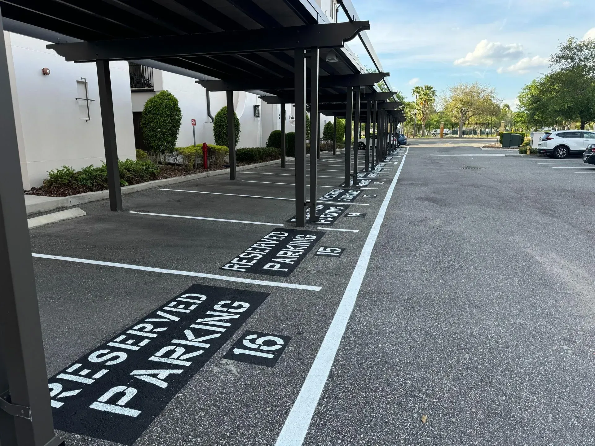 Covered reserved parking spaces under a black canopy beside a white building, marked with painted text.
