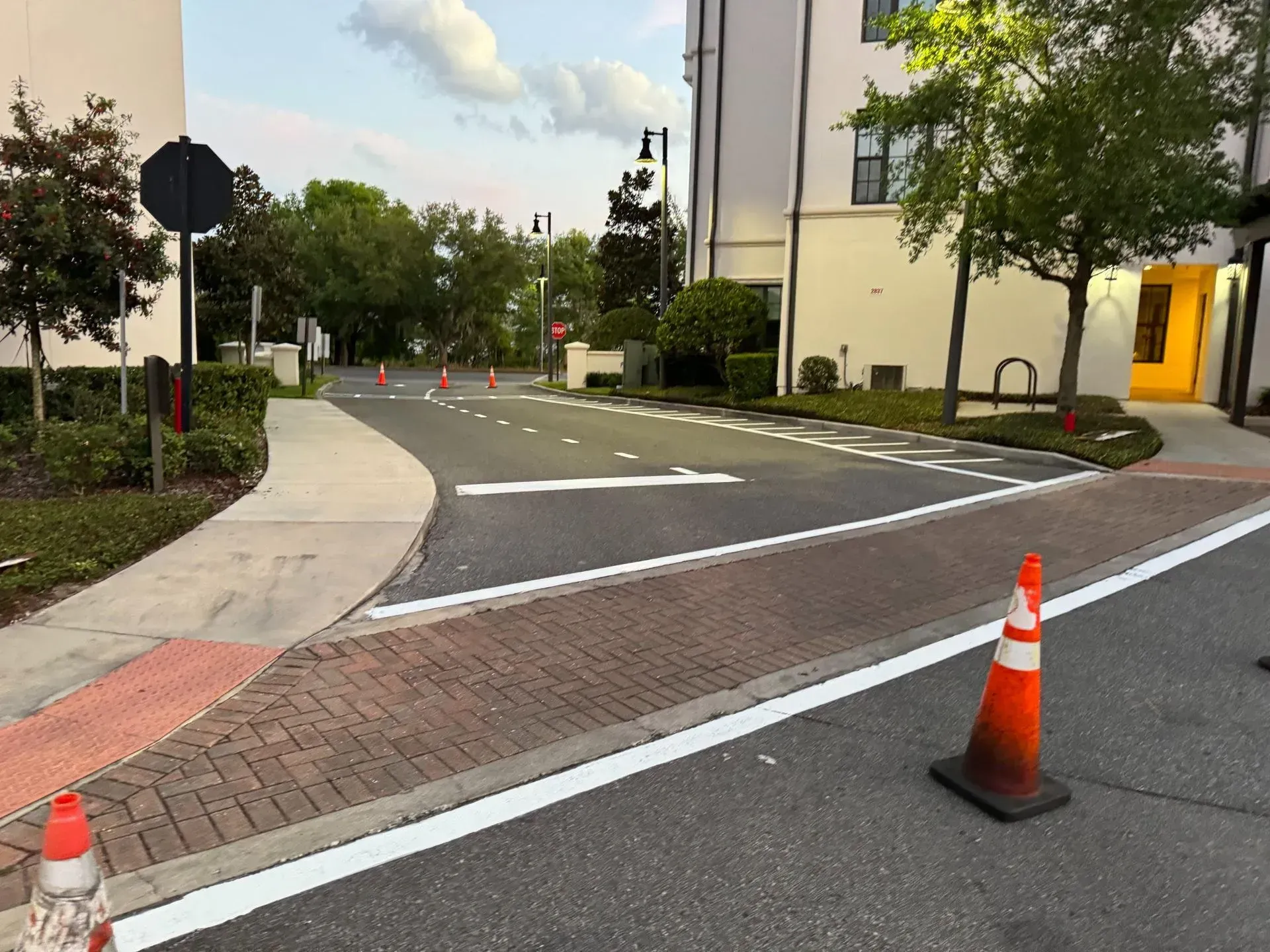 Traffic cones blocking a curved driveway beside a building and sidewalk at dusk