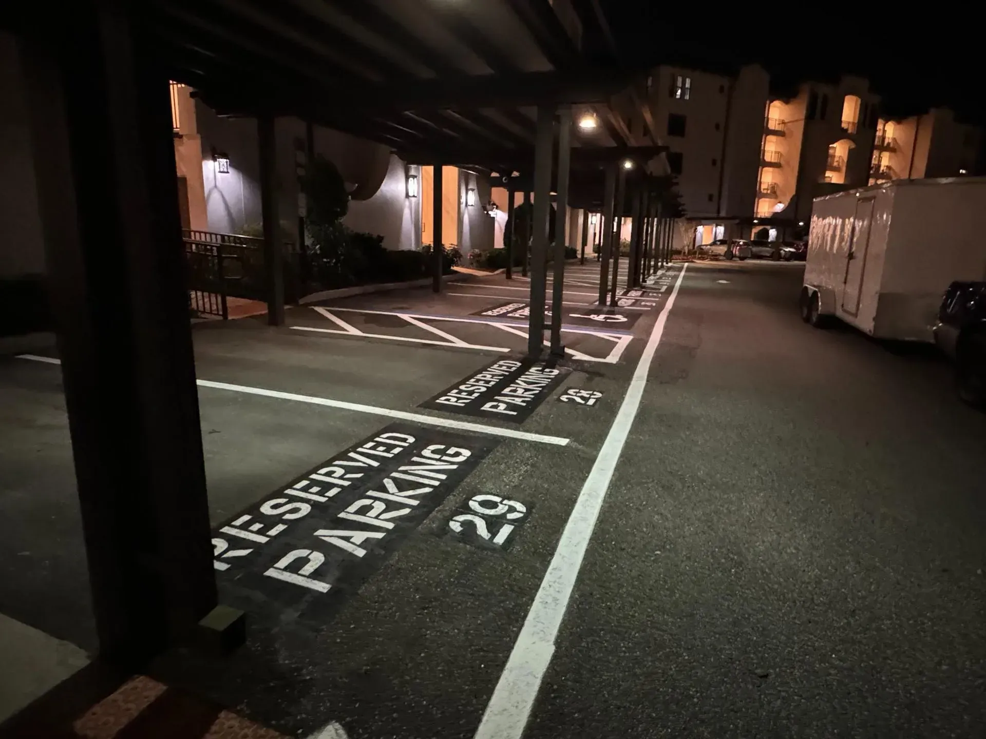 Nighttime parking lot with marked empty spaces and bright overhead lights along a covered walkway