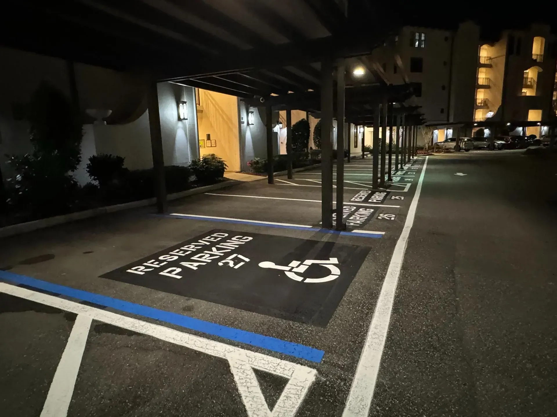 Nighttime accessible parking spaces under a covered building entrance, marked in white and blue.