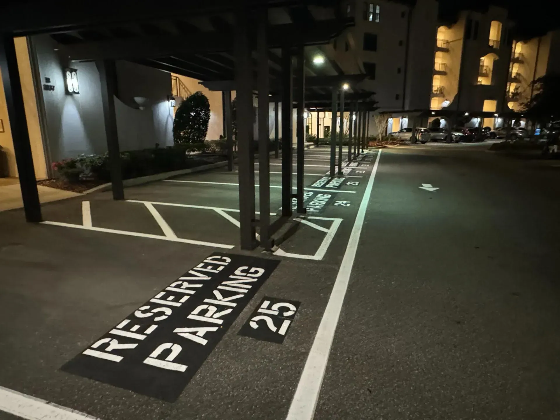 Nighttime apartment parking lot with marked reserved spaces and white lines near a building entrance