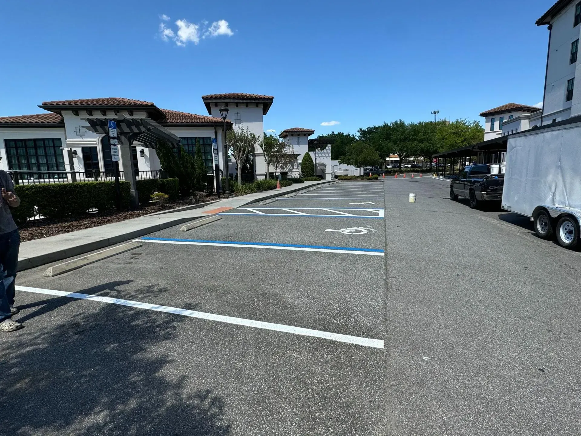 Empty parking lot beside white stucco buildings under a clear blue sky, with trailer on the right.