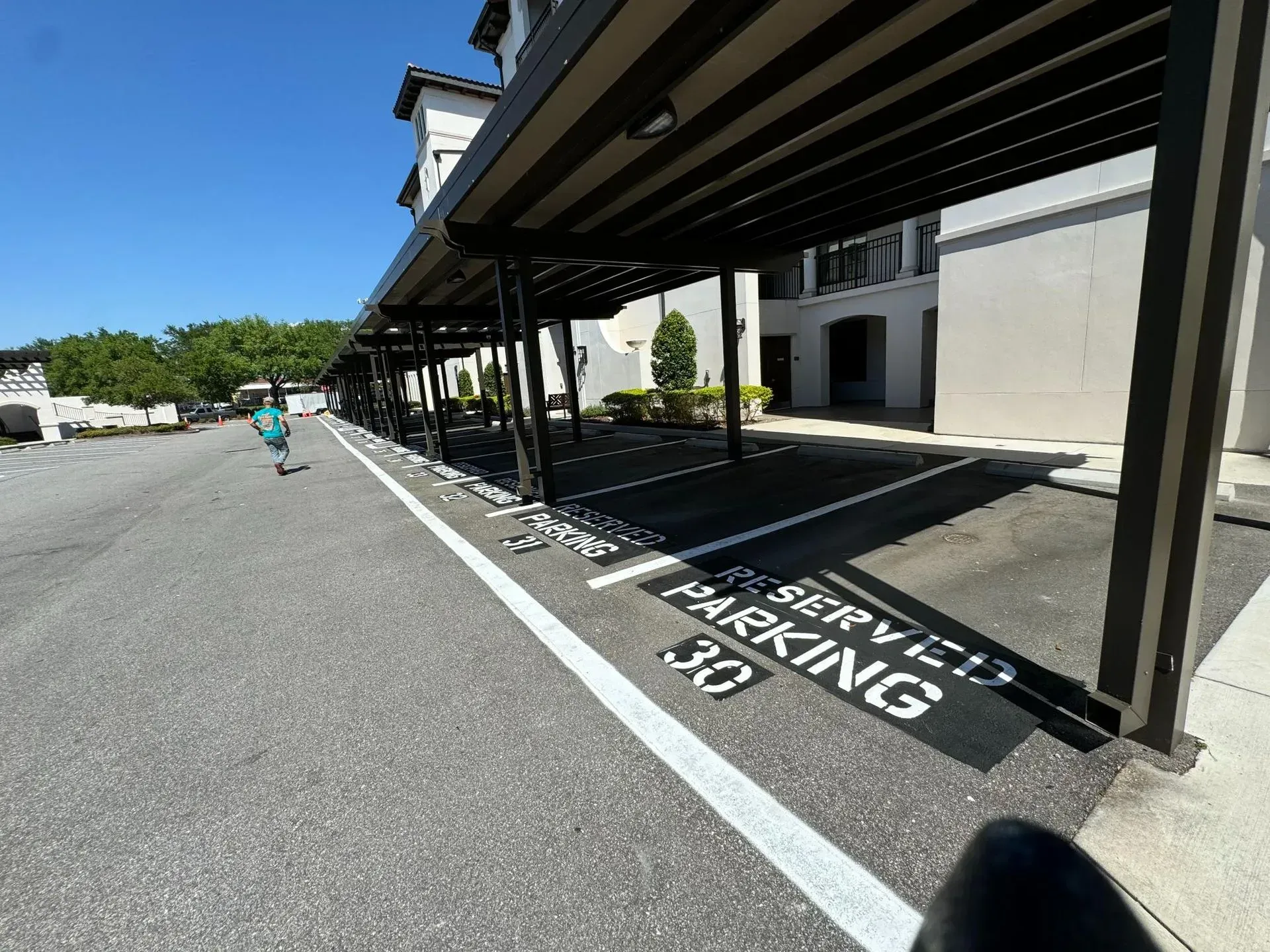 Covered parking spaces marked “Visitor Parking” beside a building, with one person walking in the distance.