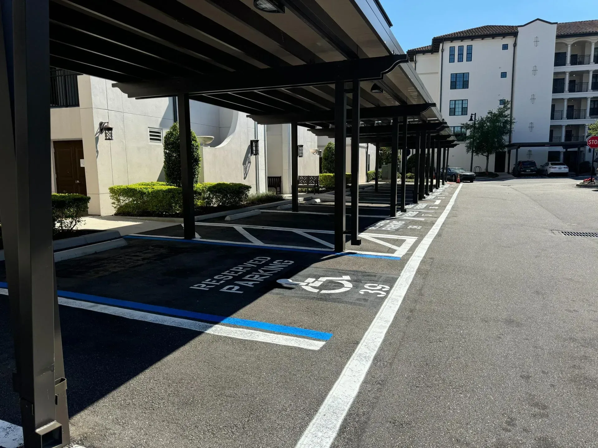 Covered parking lot with marked accessible spaces beside apartment buildings in bright sunlight