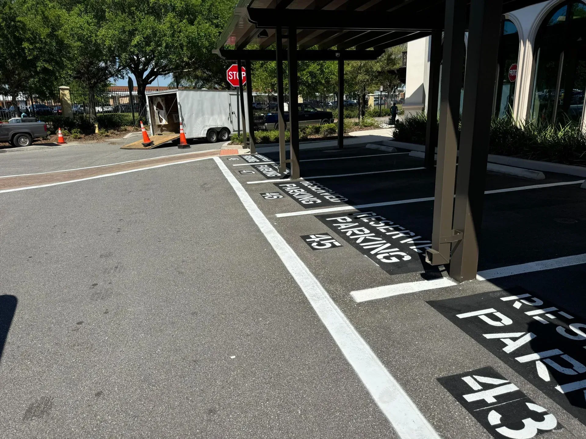 Marked parking spaces and covered walkway beside a building, with trees and street visible.