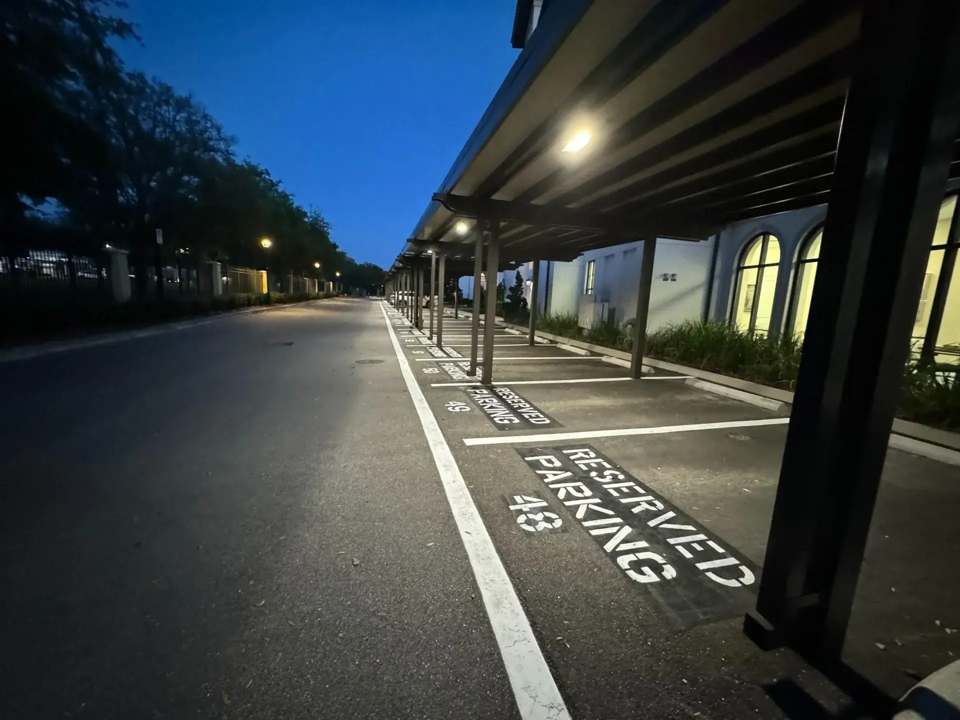 Empty nighttime parking lane beside a lit covered walkway, with “reserved parking” painted on the pavement.