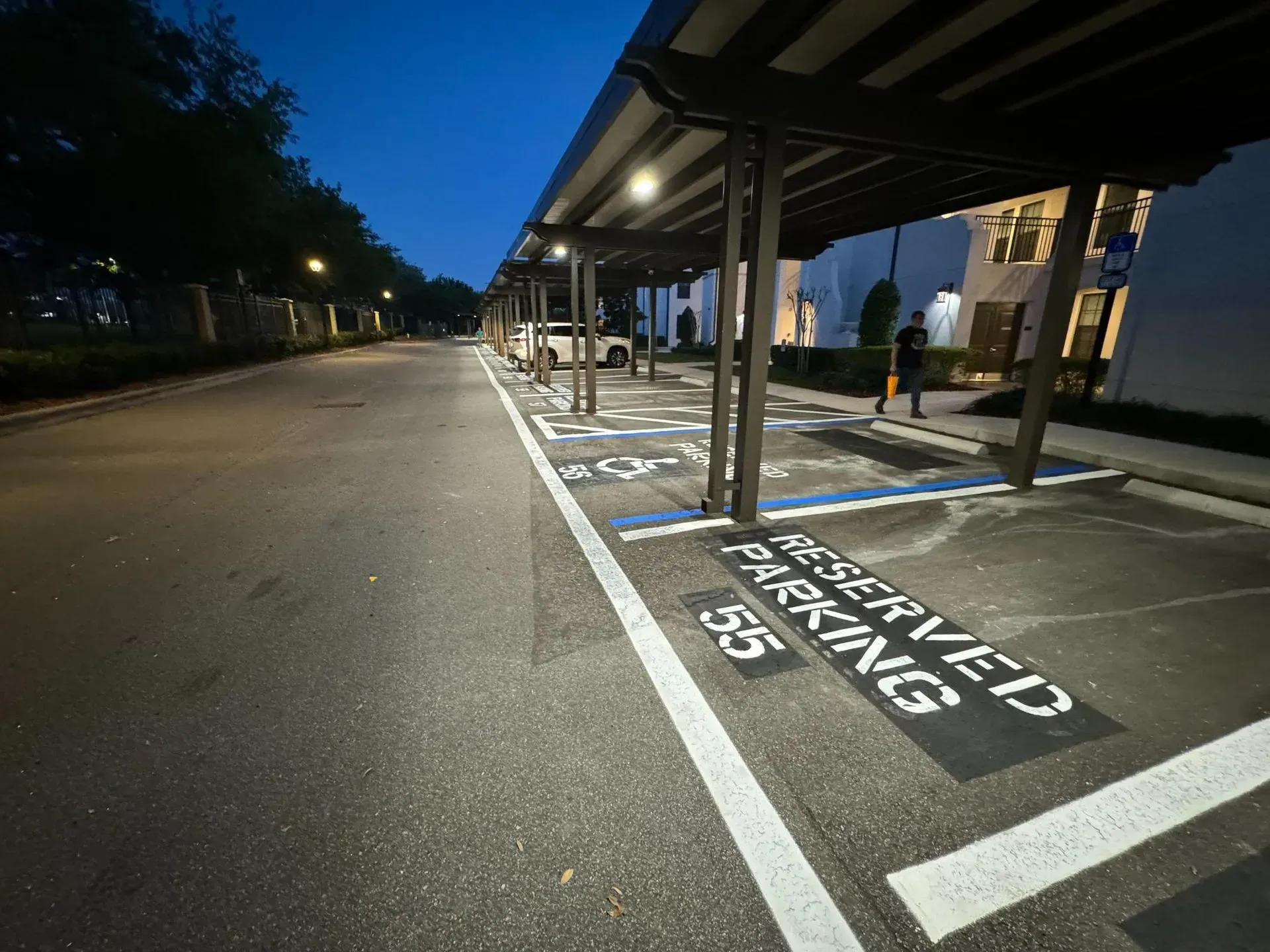 Covered parking lot at dusk with marked accessible parking spaces and a person walking near the building.