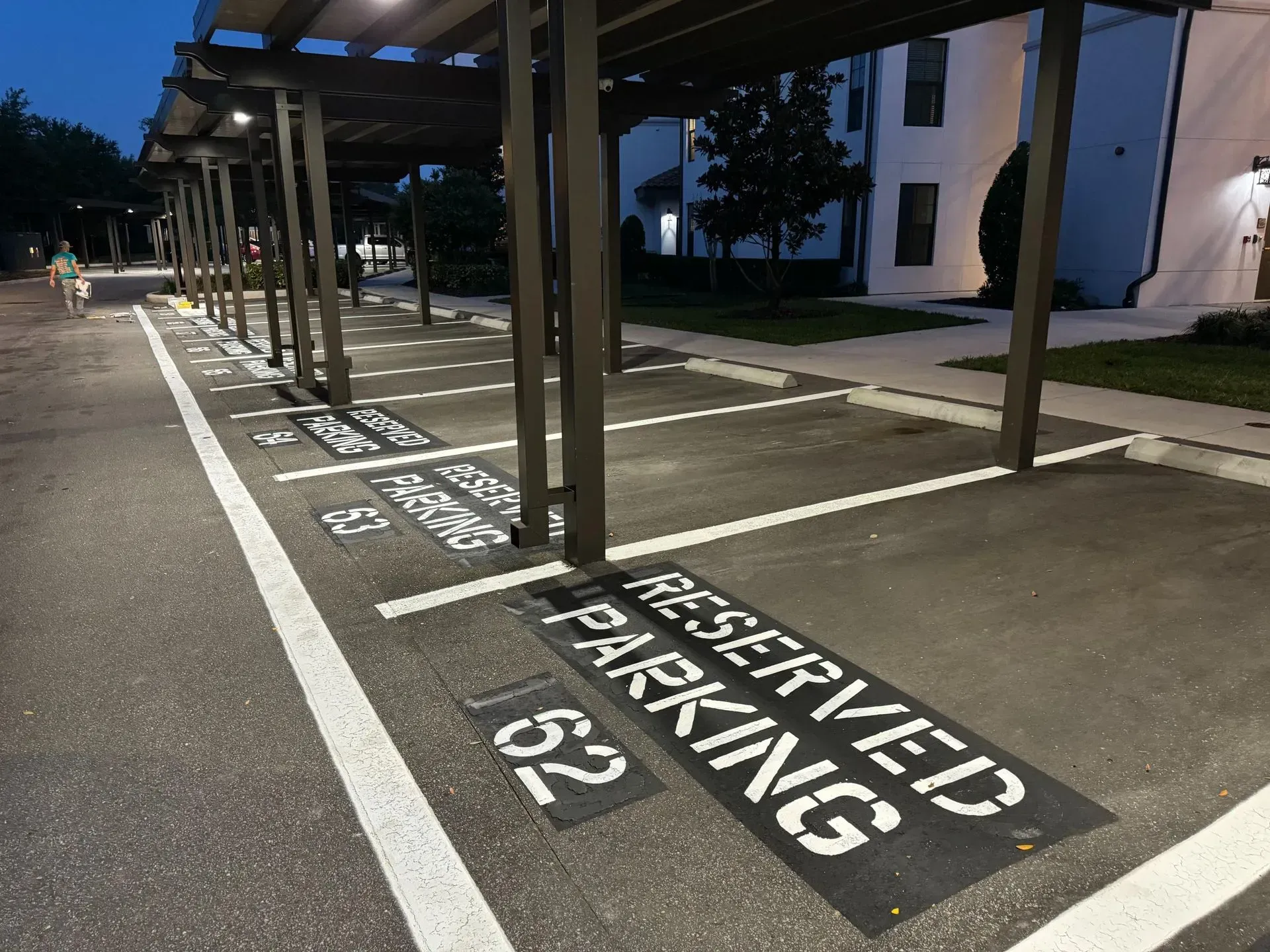 Covered parking spaces at night with painted signs reading “RESERVED PARKING 53” on the pavement.