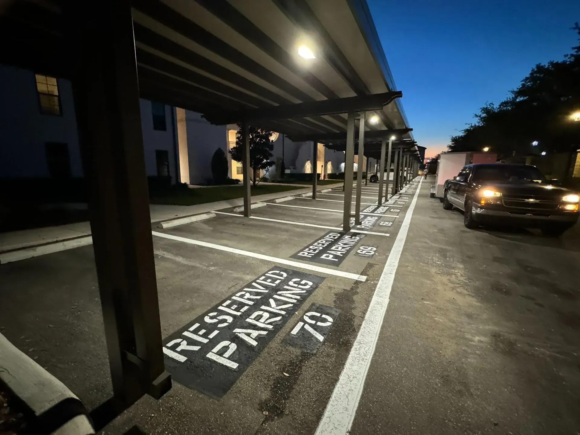 Covered parking lane marked “FRESHERS PARKING” beside a building at dusk, with cars parked along the curb.