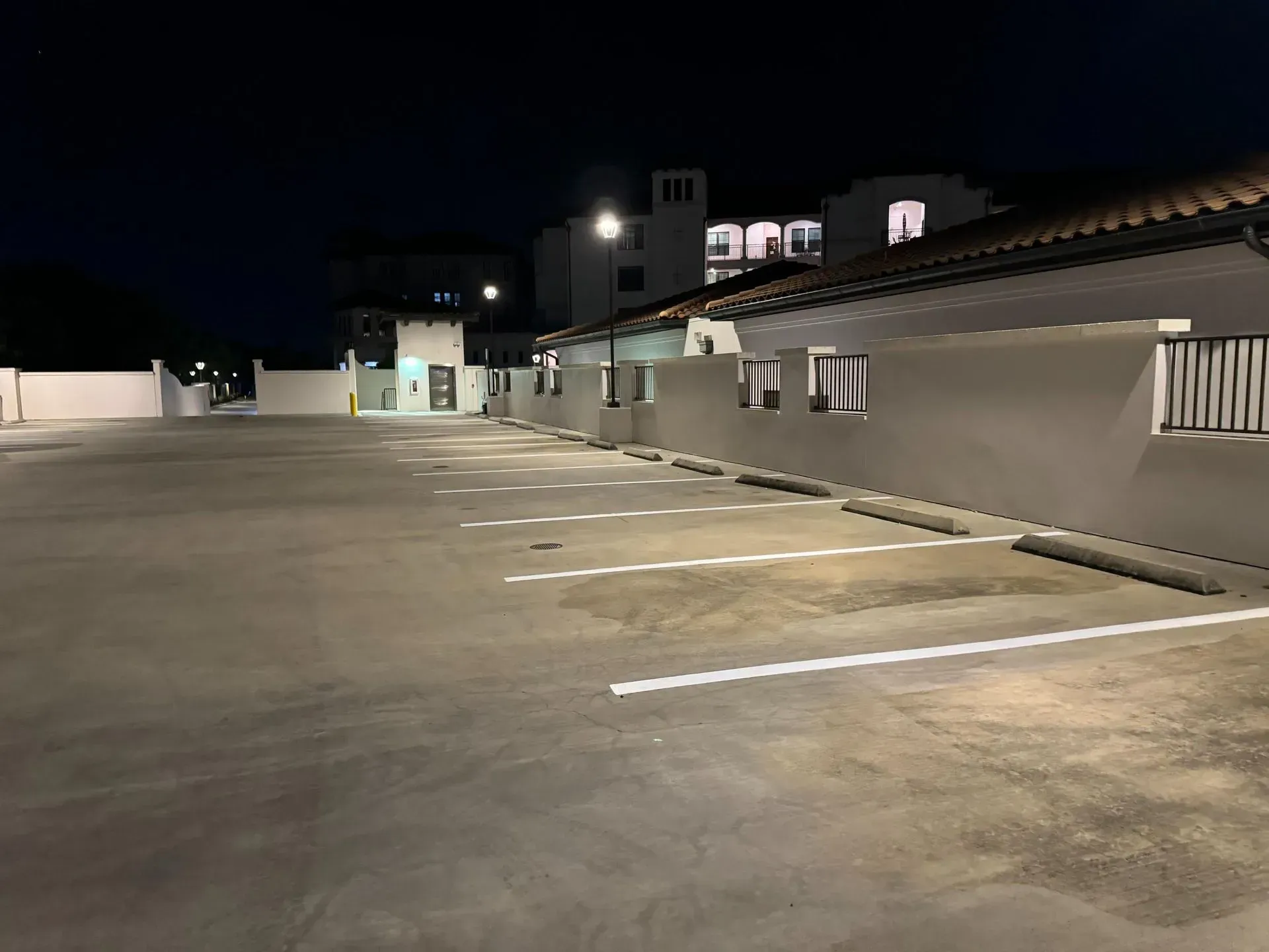 Empty rooftop parking lot at night with white parking lines and a low building along the right side.