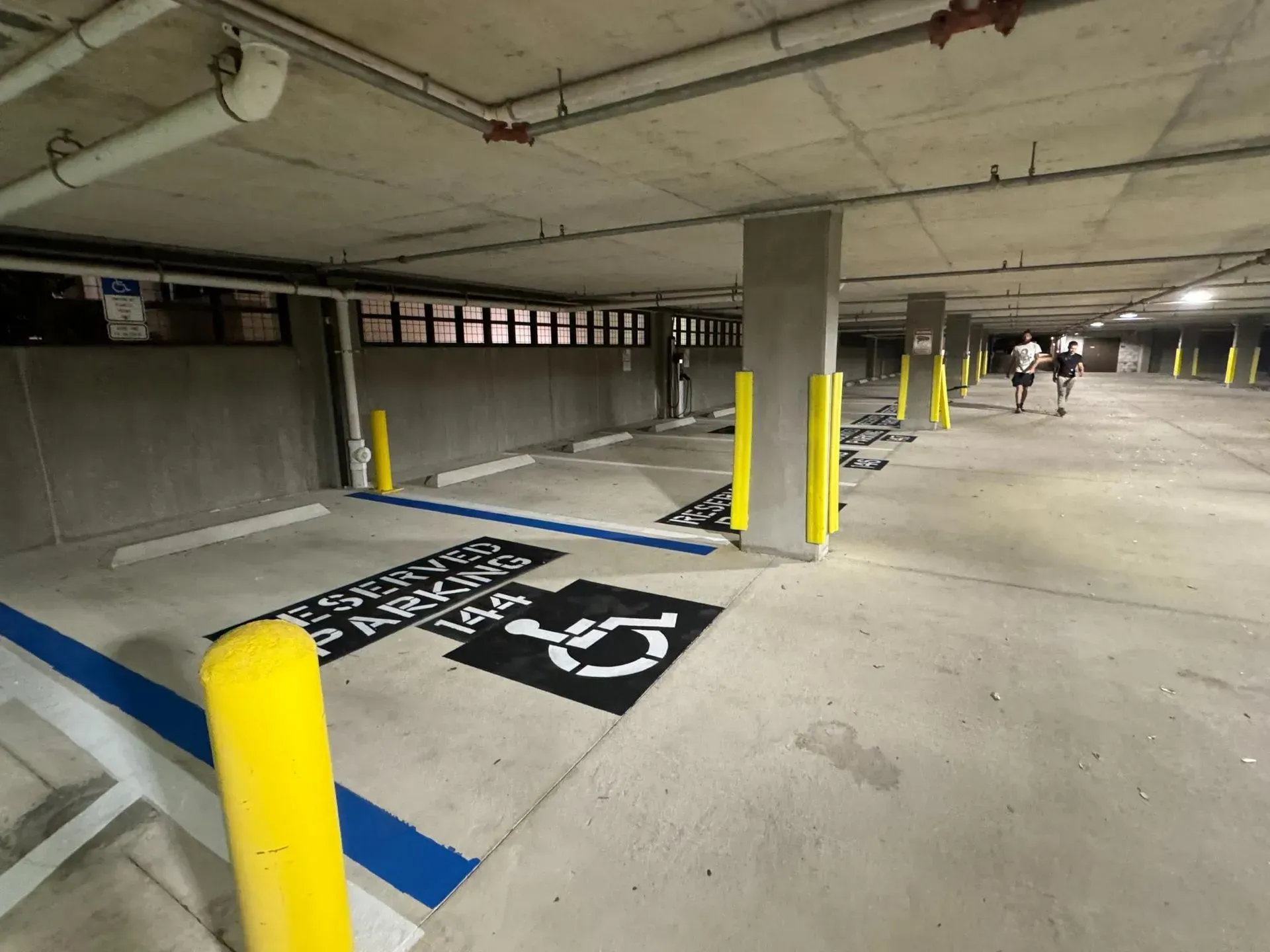 Accessible parking spaces in a concrete parking garage with yellow bollards and blue curb markings