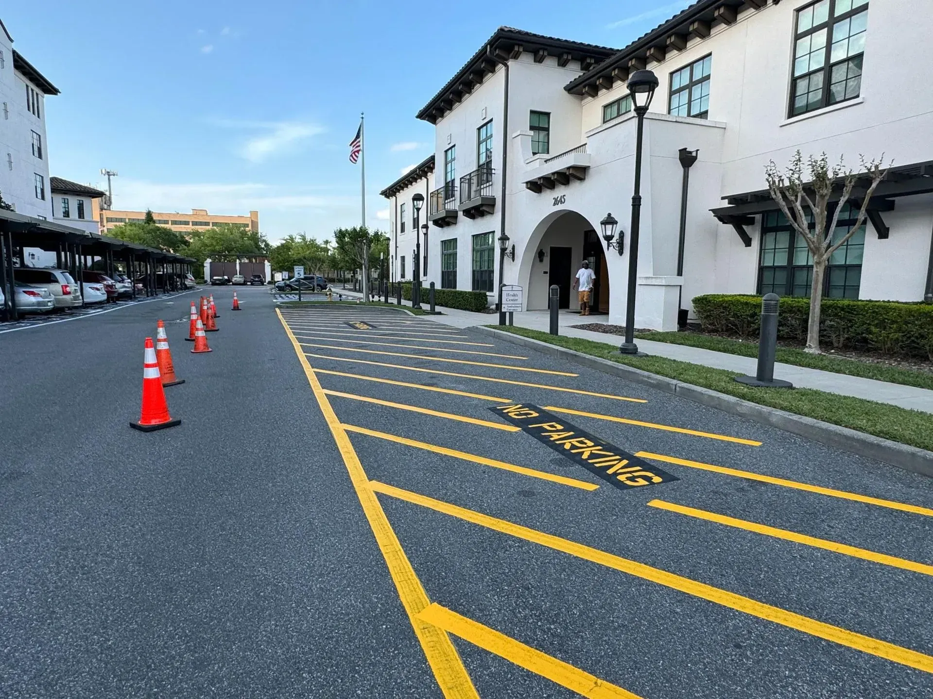 Empty street beside white buildings, with orange traffic cones and yellow road markings.