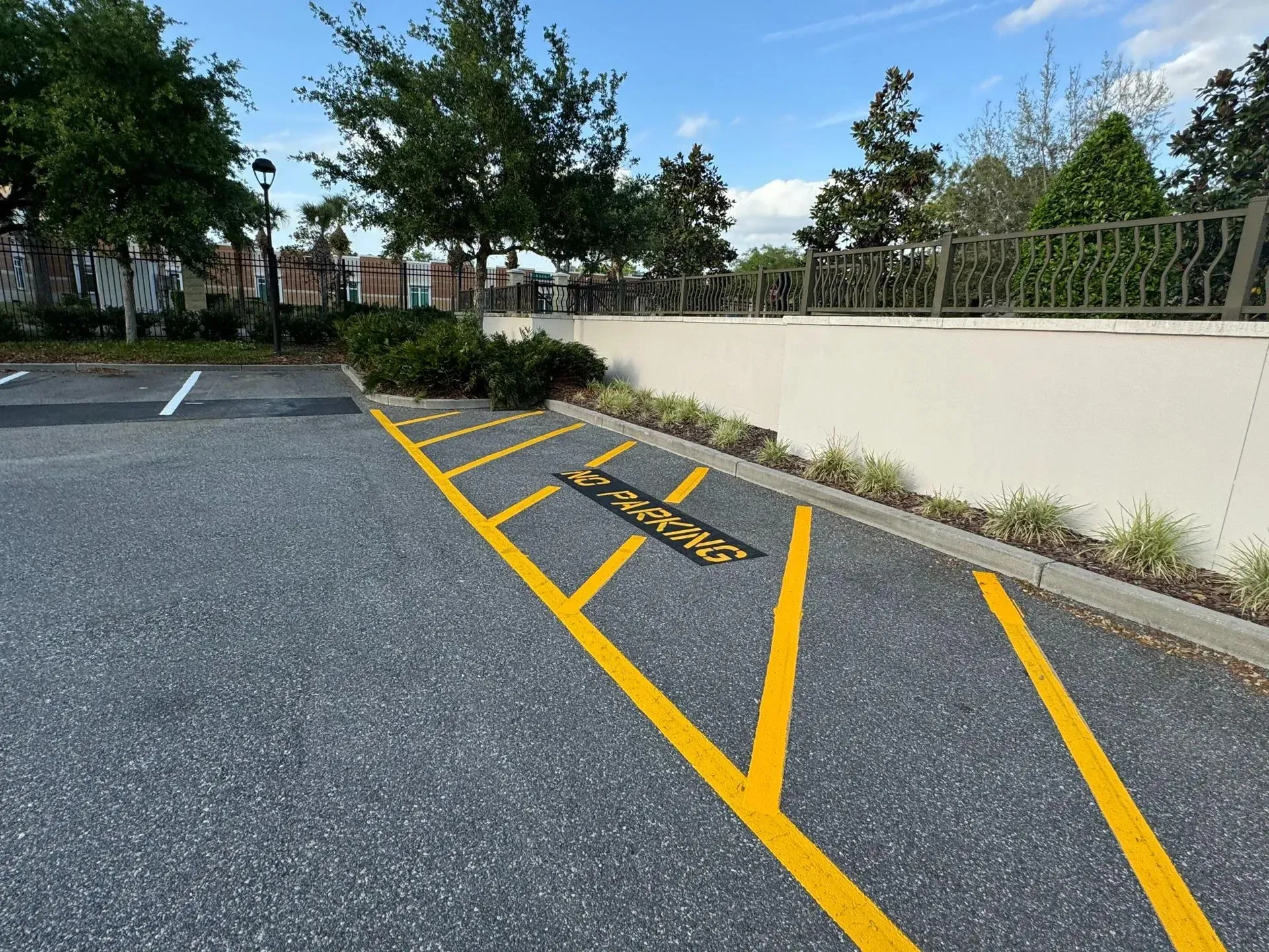 Empty parking lot with yellow no-parking lines beside a cream wall and trees